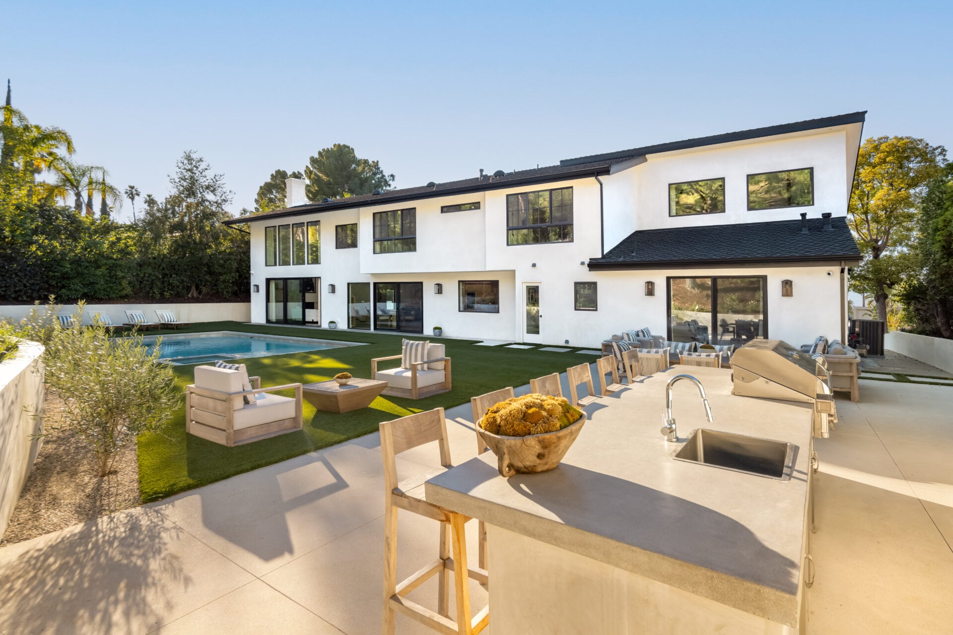 On the other side, an outdoor kitchen and bar area sit beneath the hillside, complete with built-in grilling, counter seating, and space for dining. 