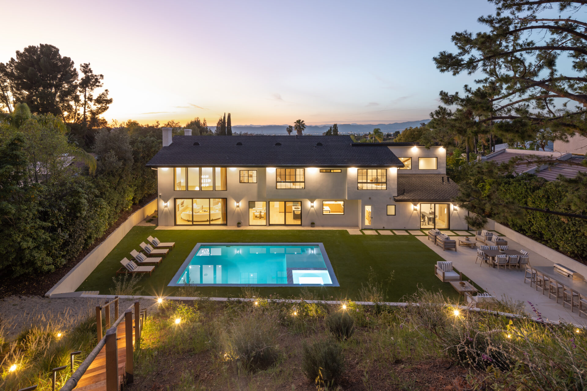The surrounding landscaping blends structured greenery with the natural slope of the hillside, where terraced planting and tall trees add depth and privacy while framing the entire yard.
