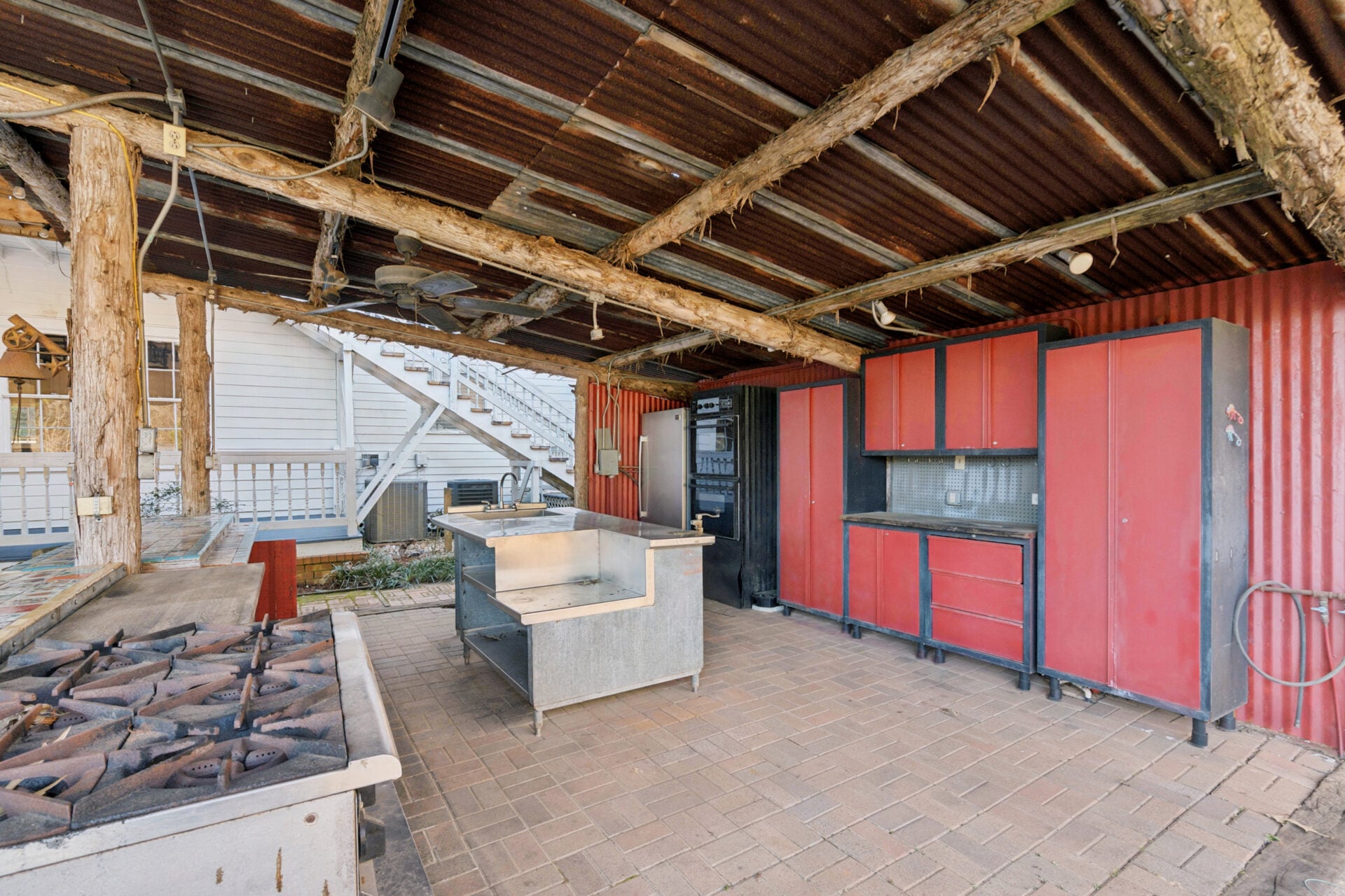 A covered section houses a fully equipped outdoor kitchen, featuring built-in appliances, prep space, and storage set beneath a rustic wood and metal roof structure. 