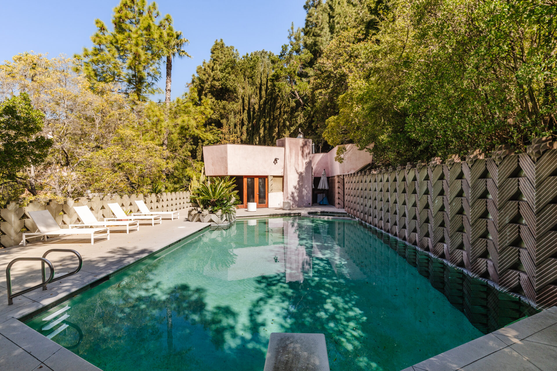 Just outside, the rectangular swimming pool stretches across the courtyard, surrounded by a wide concrete deck with space for loungers and outdoor seating. 