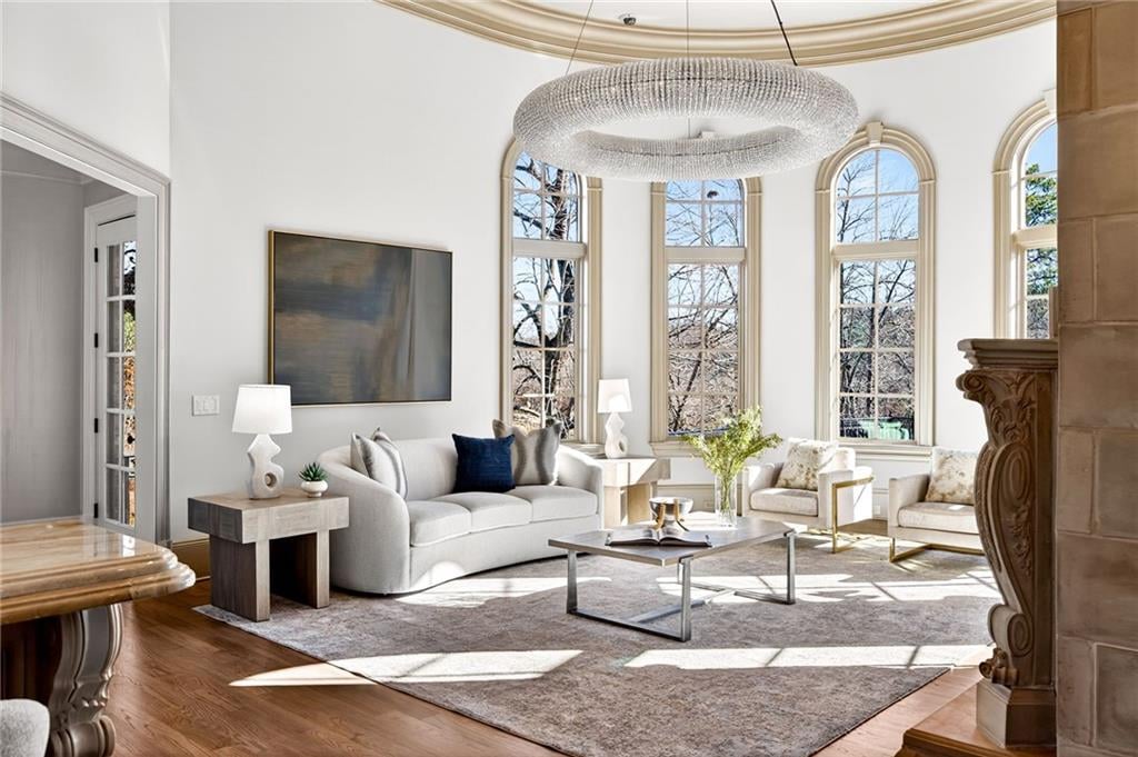 A circular recessed ceiling detail anchors the room overhead, where a sculptural crystal chandelier hangs above a neutral seating arrangement that includes a curved sofa, accent chairs, and a minimalist coffee table.