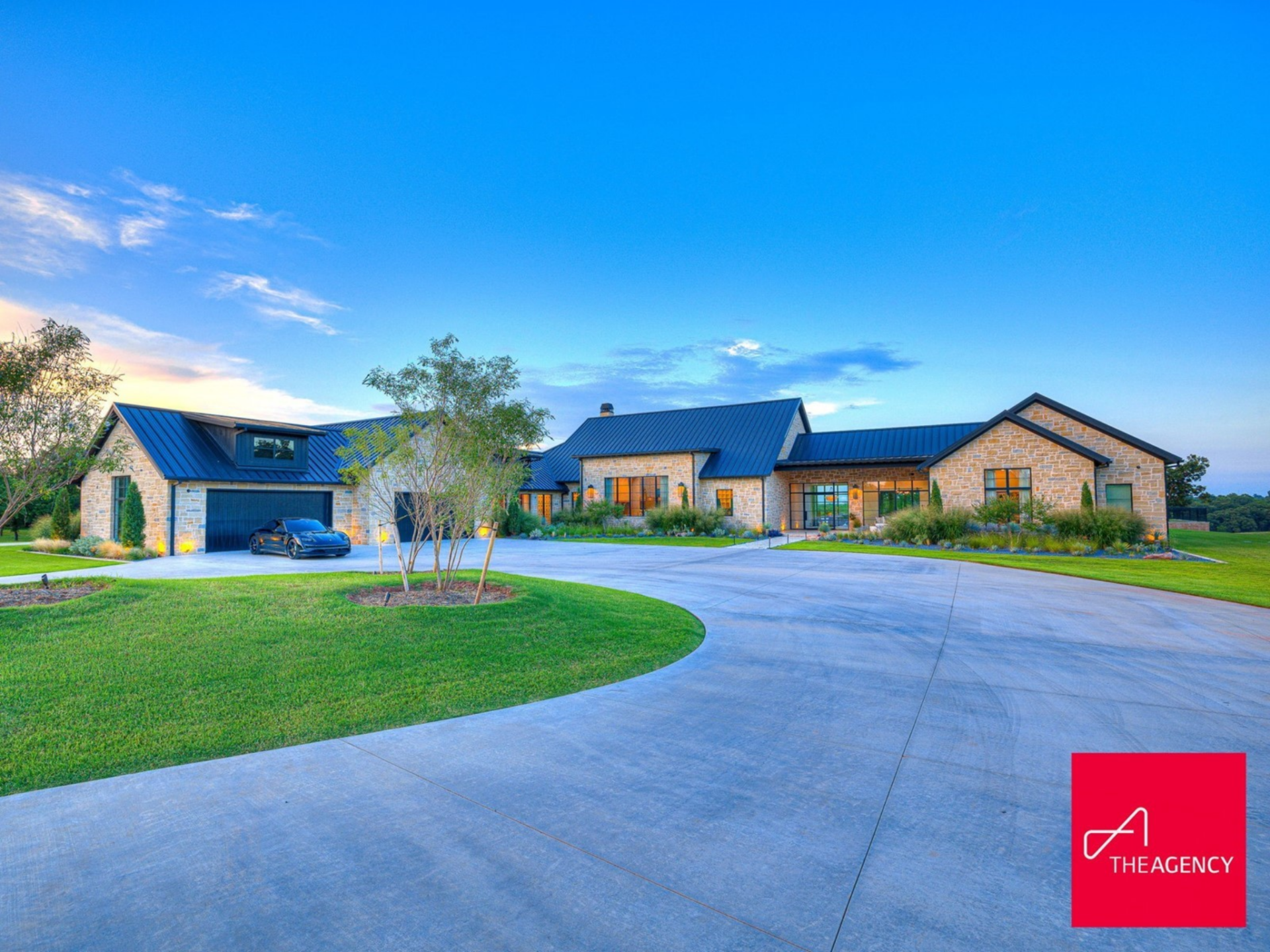 As you round the final bend, the main residence rises ahead in a Texas Hill Country style, its long, horizontal structure stretching across the landscape beneath a dark standing-seam metal roof.