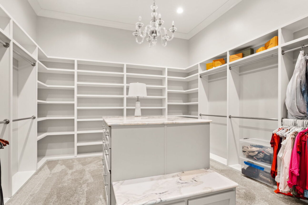 Completing the suite, the walk-in closet is designed as a full dressing room, lined with custom white shelving and hanging space on multiple walls. 