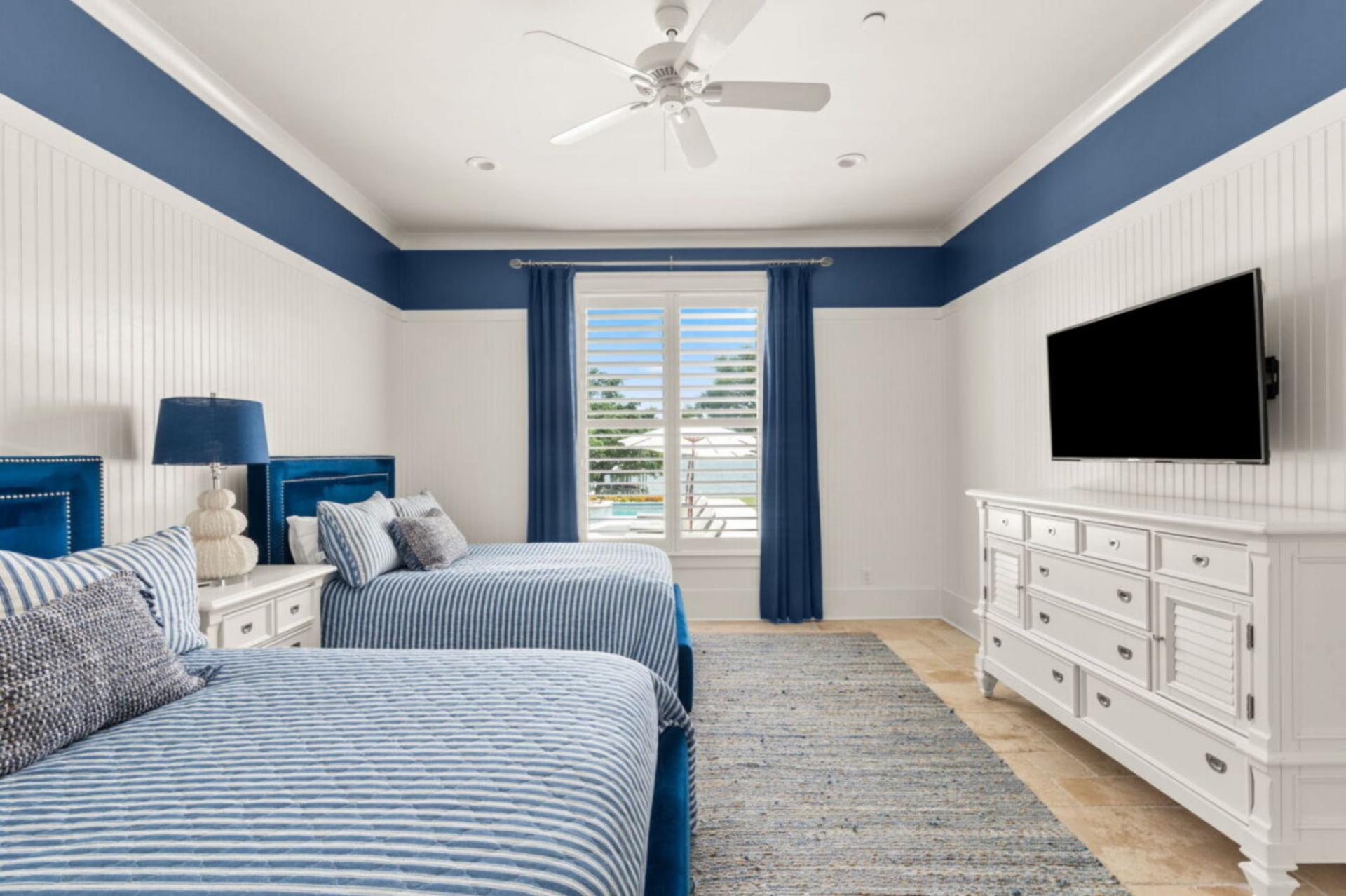 One of the guest bedrooms features a pair of twin beds upholstered in deep blue fabric, complemented by striped blue-and-white bedding and matching curtains.