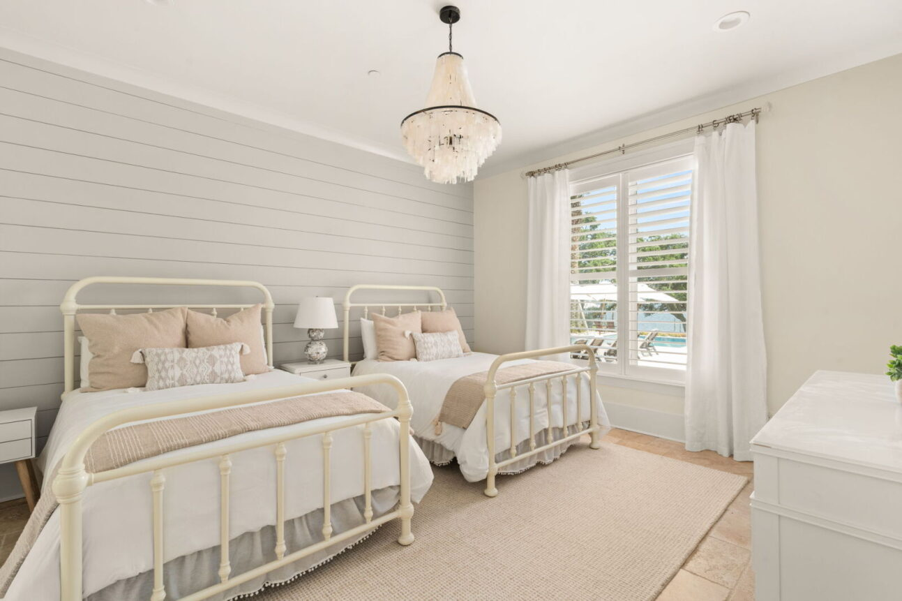 A third bedroom includes two vintage-style twin beds with white metal frames positioned beneath a crystal-style chandelier.