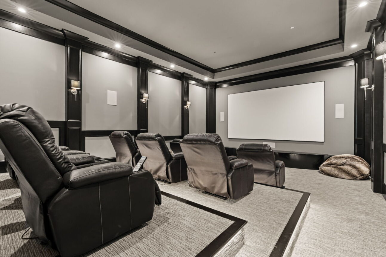 Tiered seating with leather recliners creates a true cinema-style setup, while dark trim, recessed lighting, and wall sconces give the room a classic theater atmosphere.