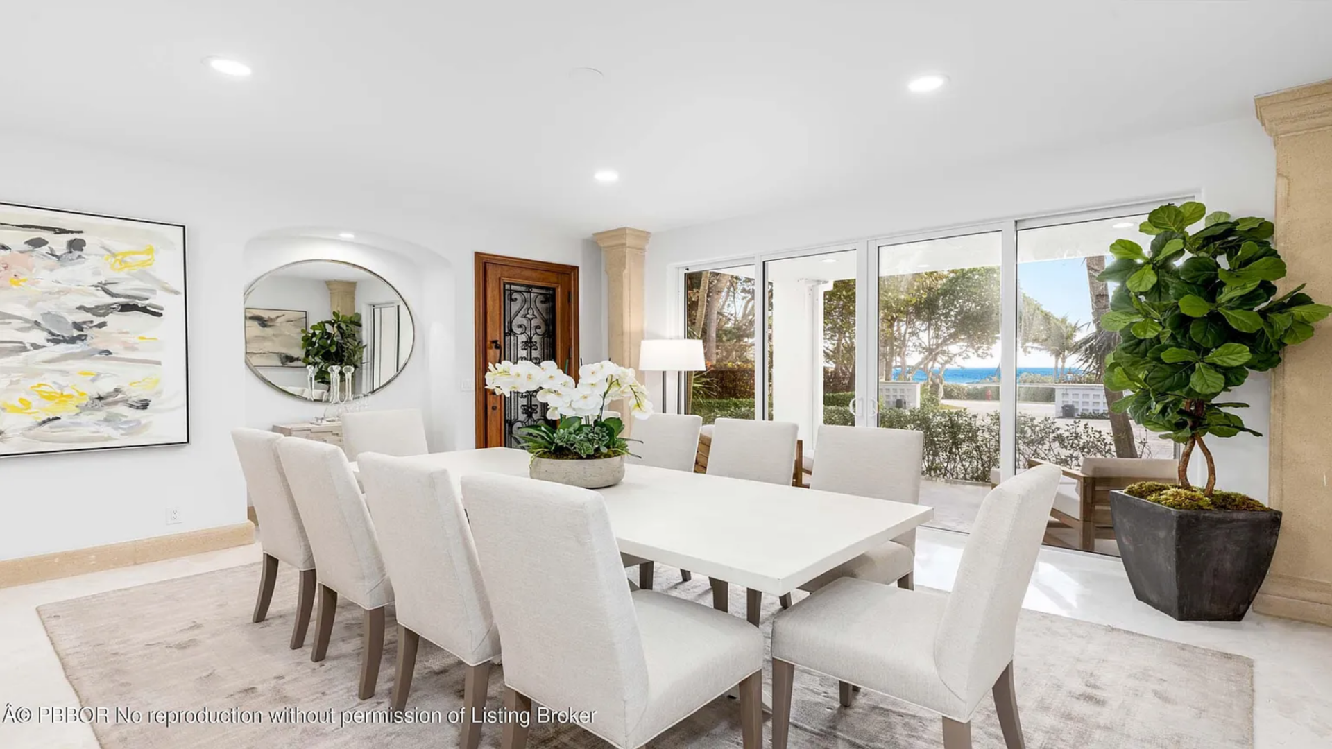 Inside, a long rectangular table sits at the center of the space, surrounded by upholstered chairs and topped with a simple arrangement of white orchids.