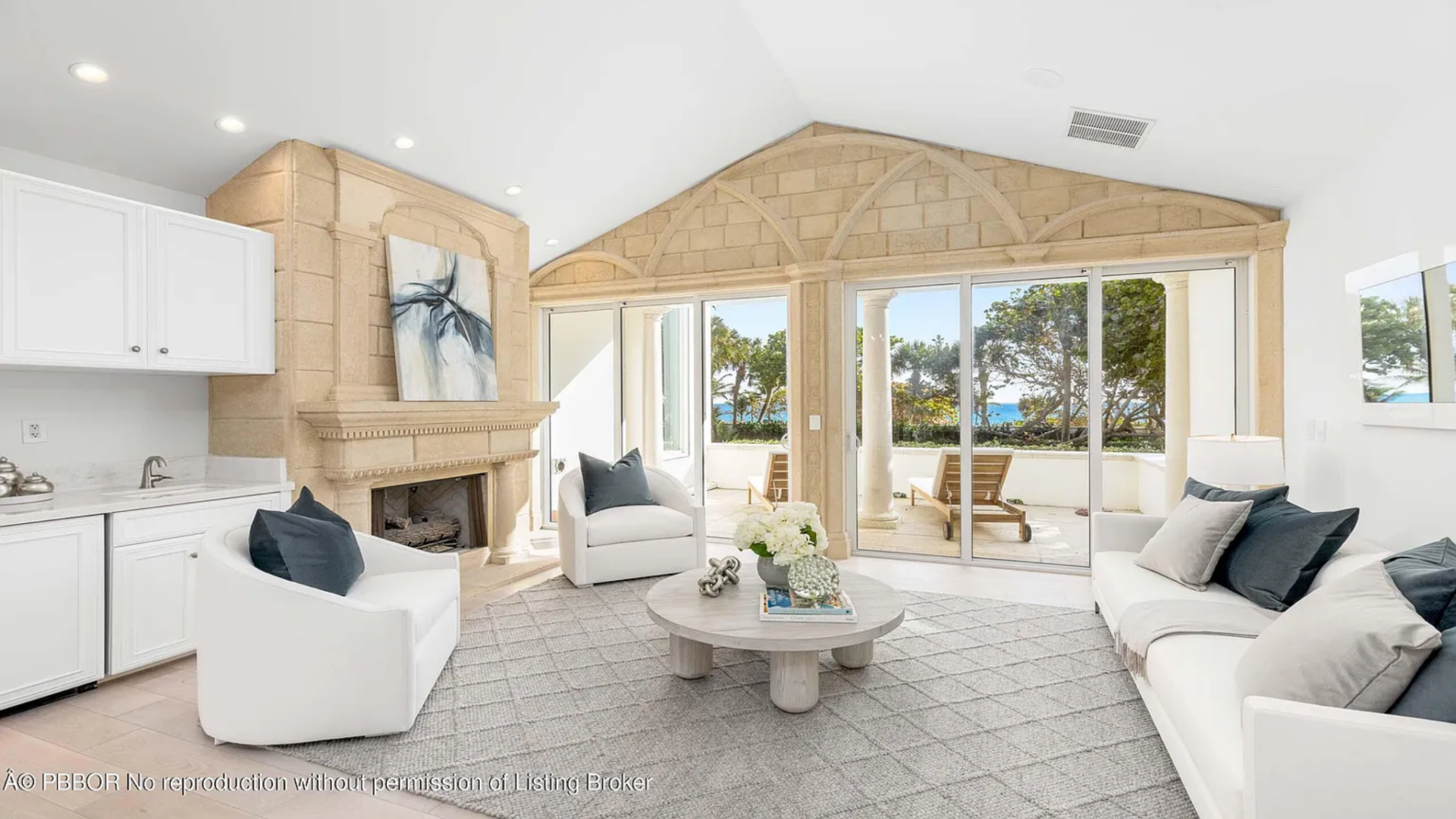 A sofa, armchairs, and a round coffee table sit on a large rug beneath a stone-clad accent wall that frames sliding glass doors leading to the balcony.