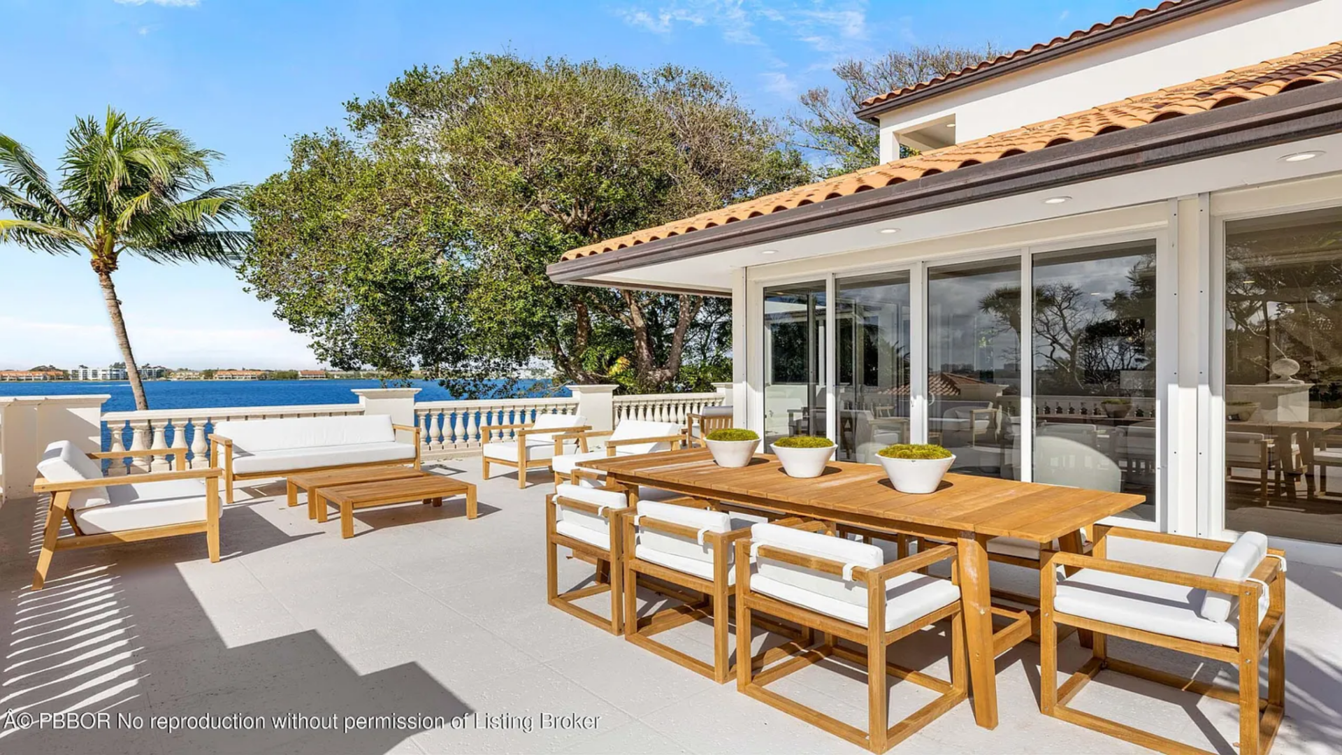 One of the most prominent spaces is the main dining terrace, where a large wood dining table and matching lounge seating sit just outside the glass doors of the home.