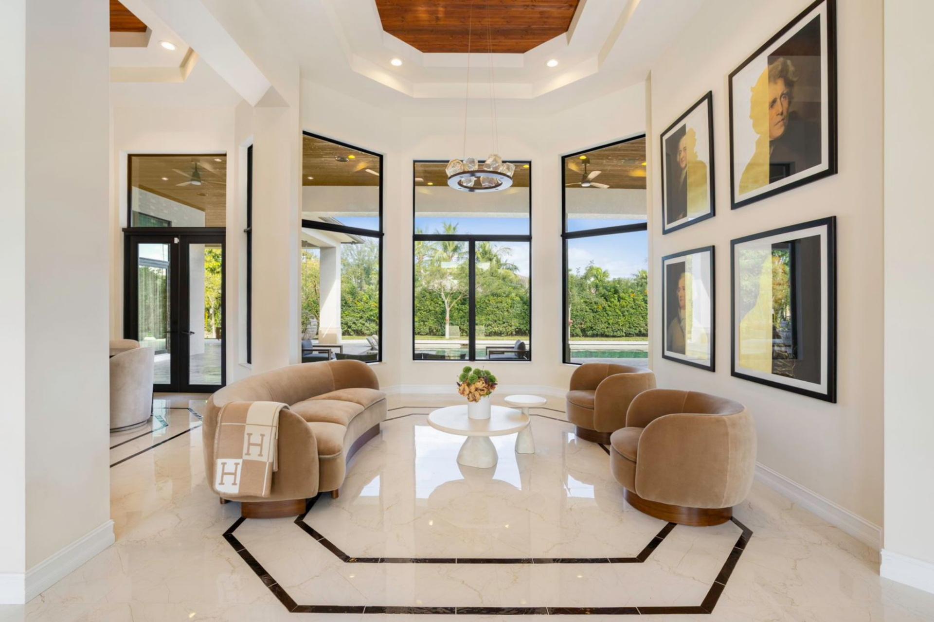 A curved sofa and a pair of rounded lounge chairs create a conversation area beneath tall windows that frame views of the surrounding greenery just outside.