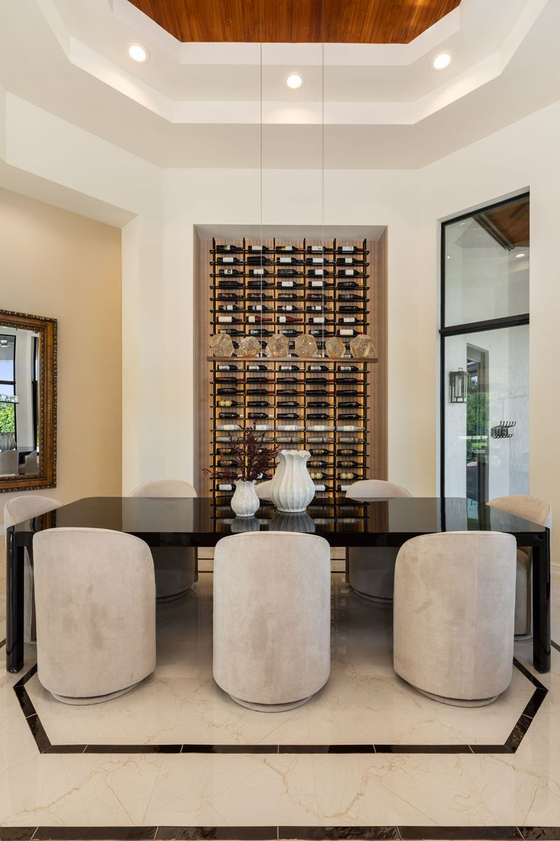 On the other side of the tall columns, the layout transitions into the formal dining area, where a long black dining table sits centered beneath the same soaring ceilings. 