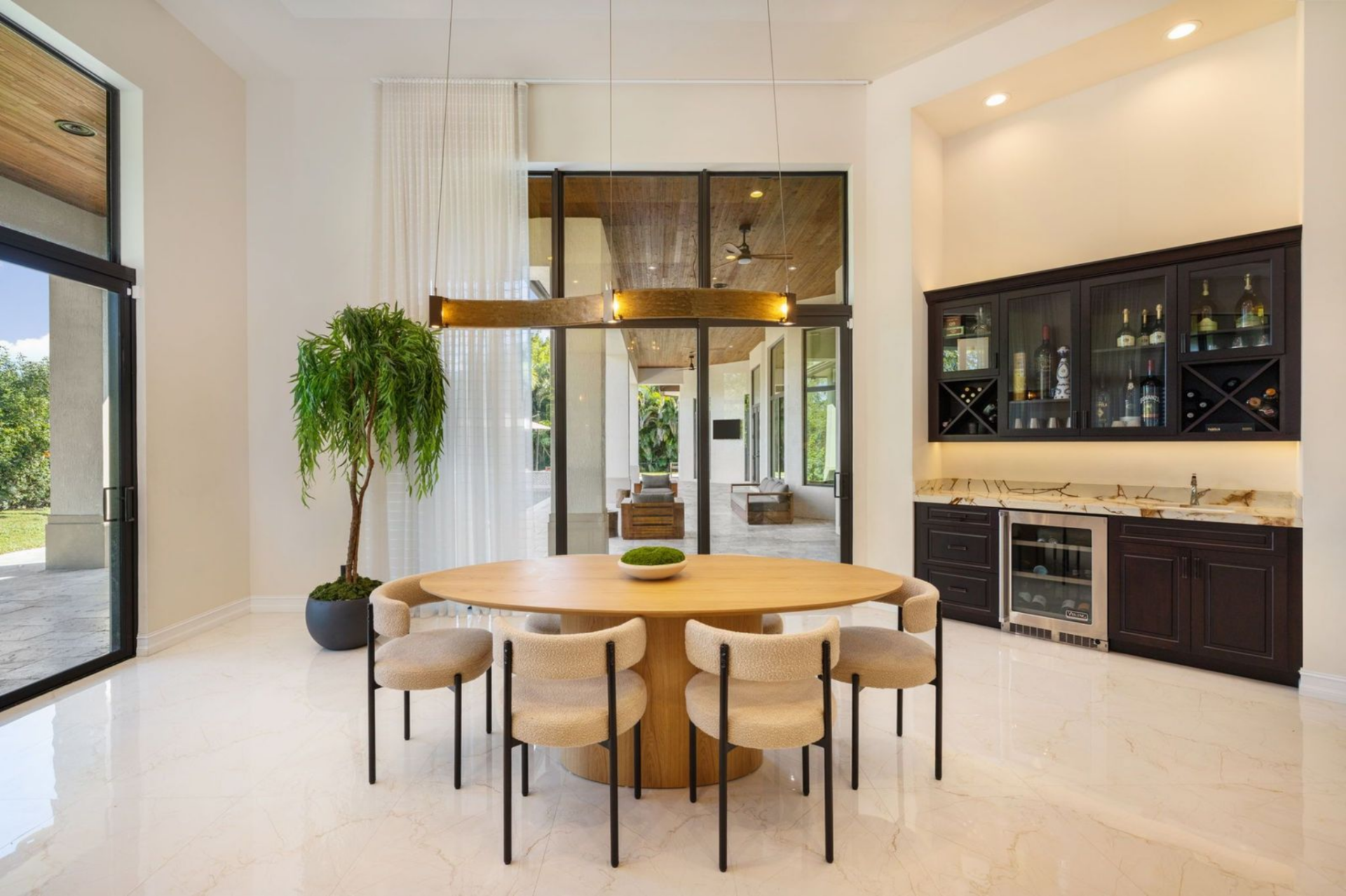 A round table sits beneath a suspended light fixture, while a built-in wet bar and wine cooler line the wall nearby, adding another layer of functionality for entertaining.