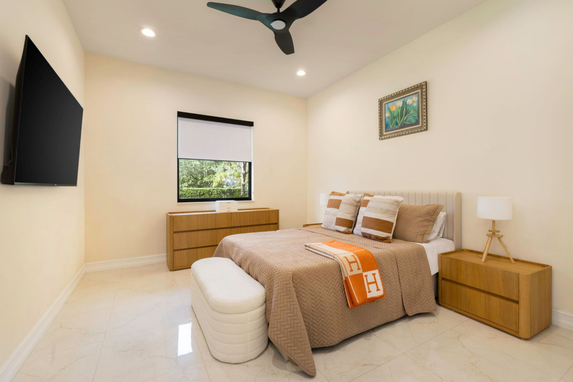One of the guest bedrooms features a warm neutral palette centered around a light upholstered bed layered with textured bedding and accent pillows. 