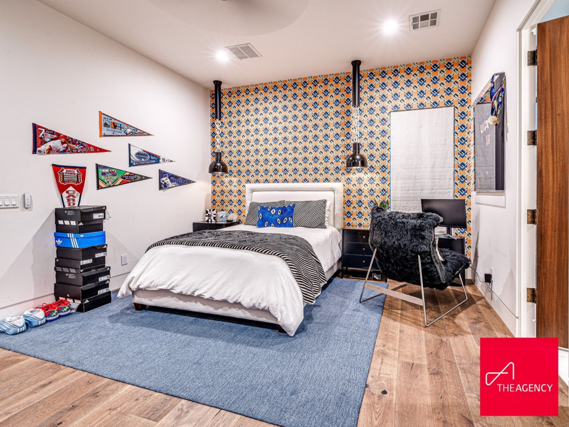 A bold patterned accent wall sits behind the bed, framed by sleek black pendant lights that hang from the ceiling on either side.