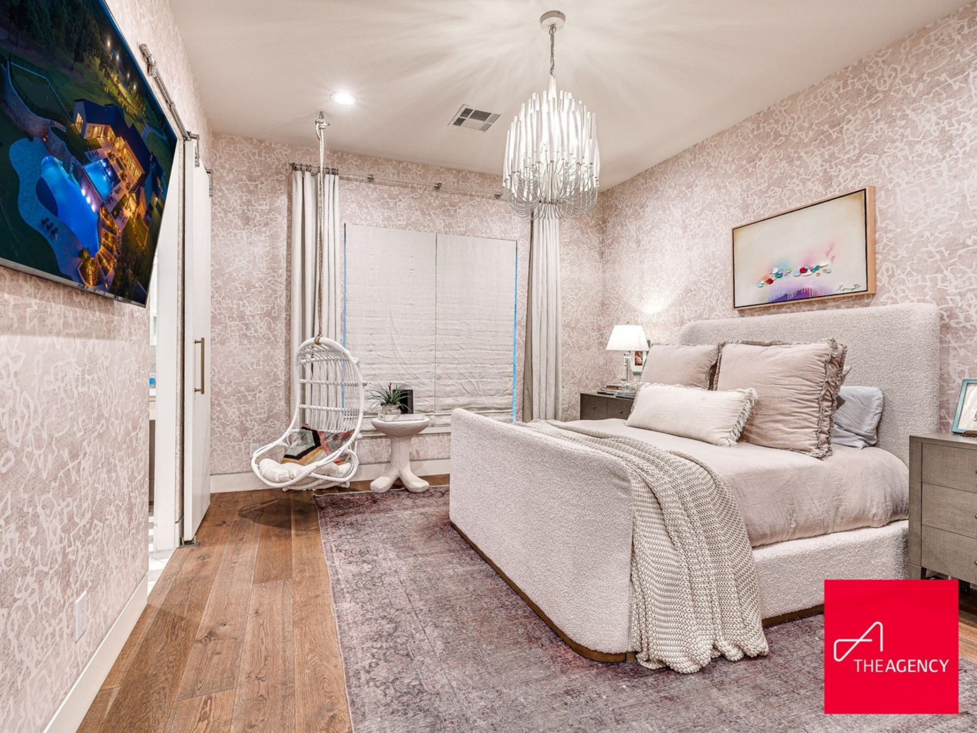 Wrapped in subtly patterned wallpaper, the room features a plush upholstered bed that sits centered beneath a framed artwork, while a hanging chair tucked near the window adds a playful but polished detail.