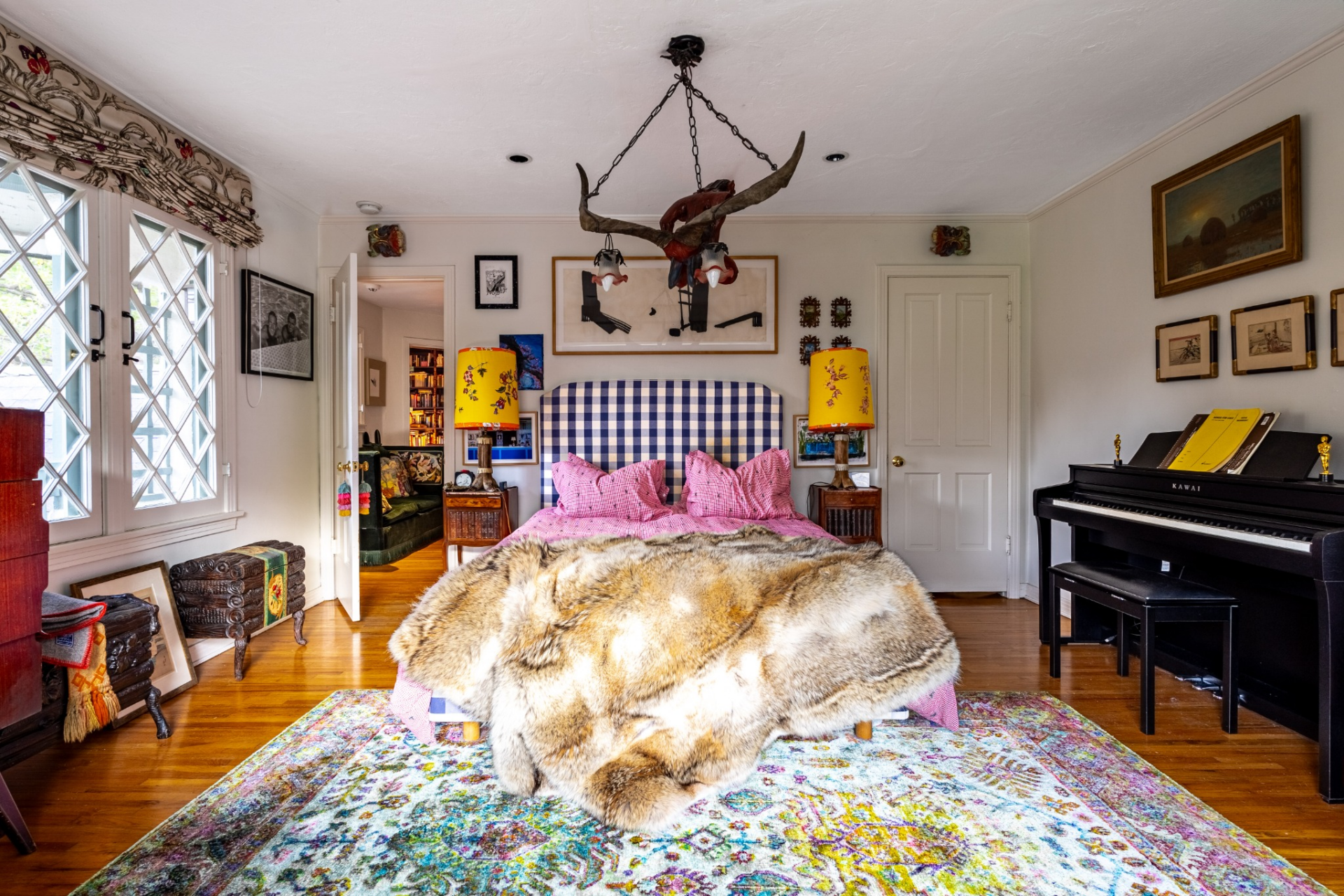 At the center of the bedroom, a bed with a blue checkered headboard and pink bedding sits beneath a dramatic chandelier crafted in an antler shape.