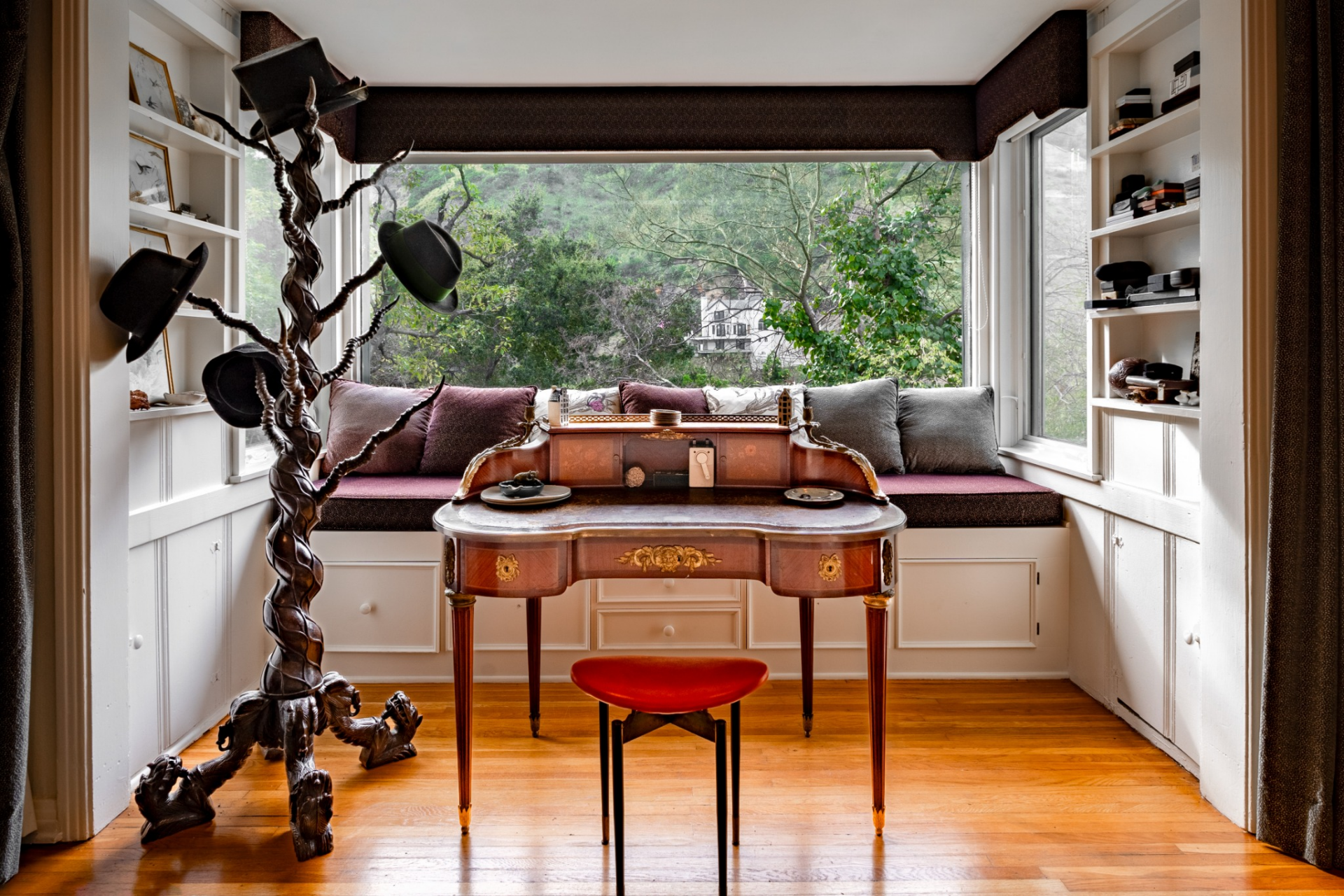 A built-in bench with cushions creates a quiet place to sit, while a vintage writing desk and shelves tucked along the sides turn the corner into a compact workspace filled with natural light.