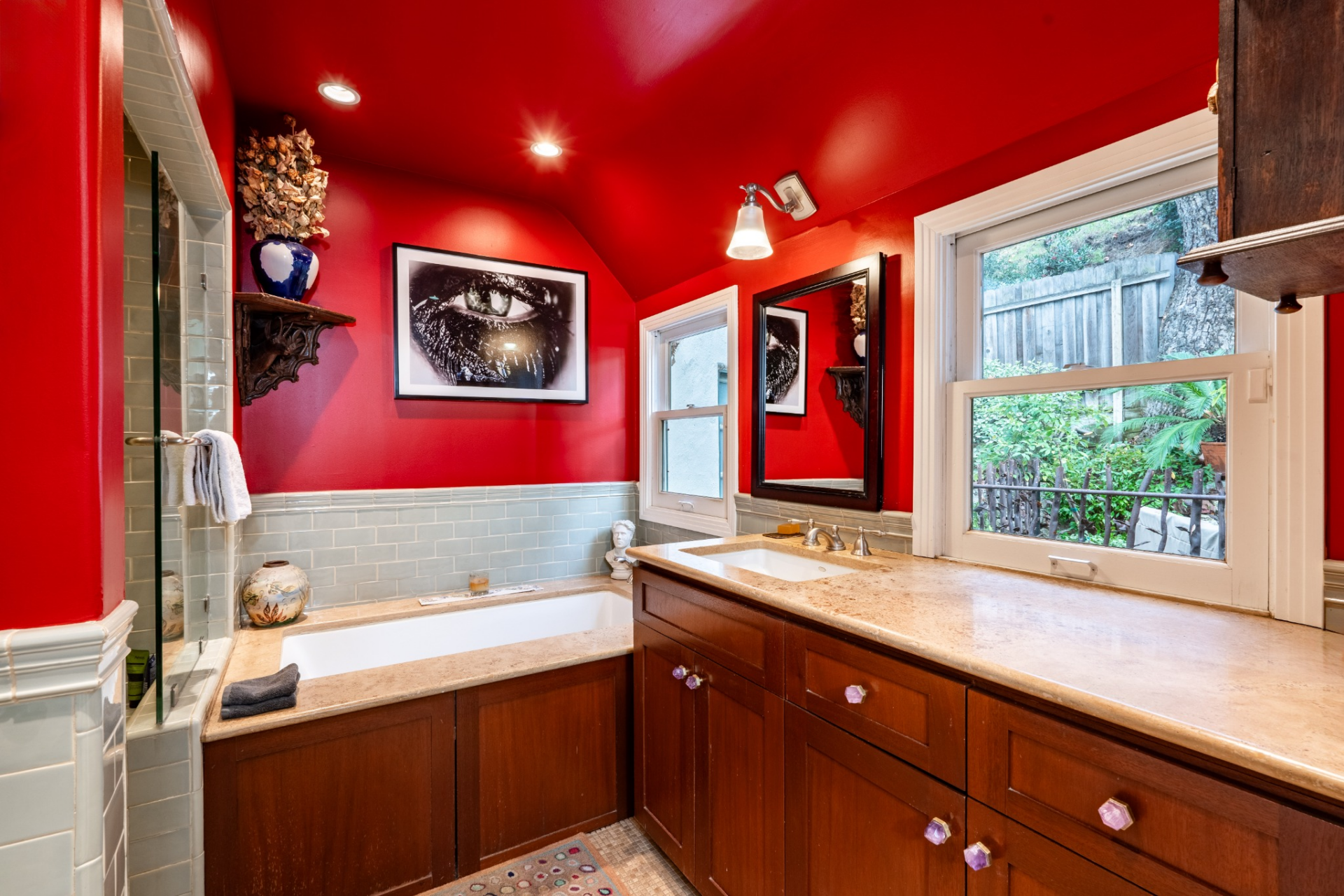 The primary bathroom continues the bold color palette with bright red walls paired with light blue tile and warm wood cabinetry.