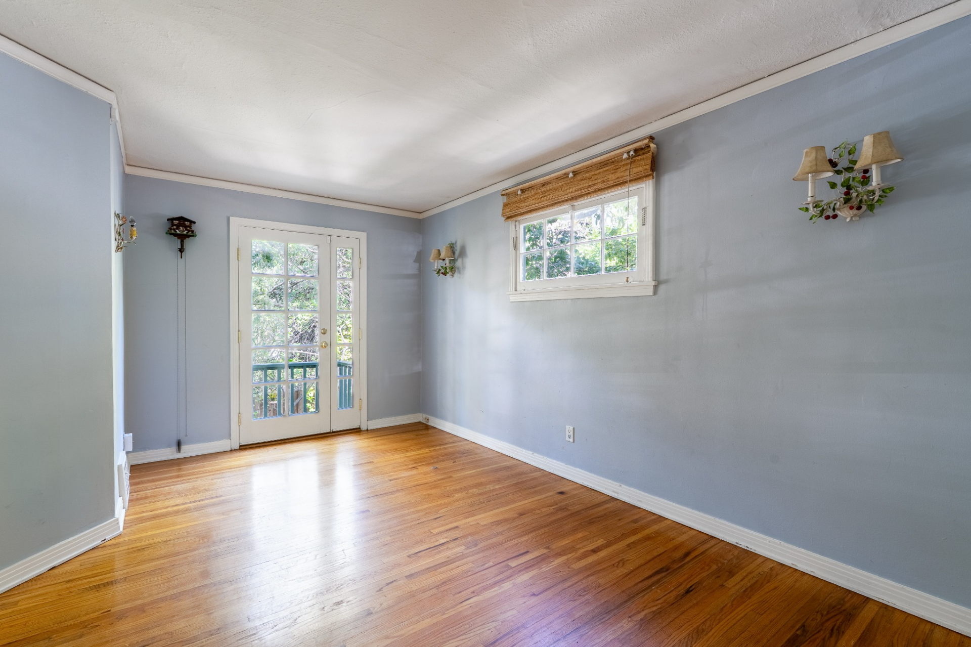 This room features hardwood floors and soft blue walls, with a door that opens directly onto a small balcony overlooking the surrounding greenery.