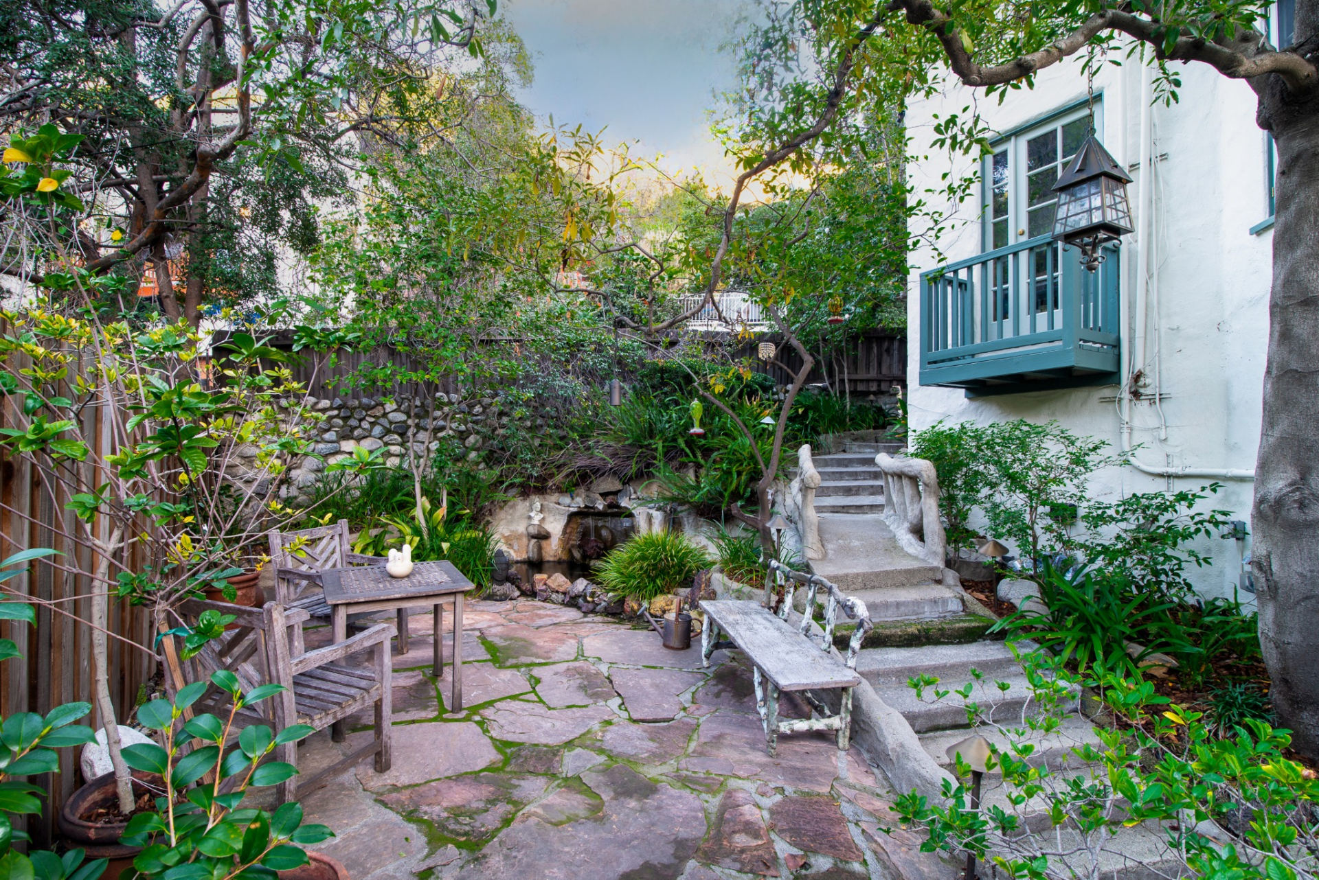 One of the more distinctive features here is the small decorative “lover’s bridge,” which crosses over a water feature along the patio and adds a whimsical touch to the layered outdoor layout.