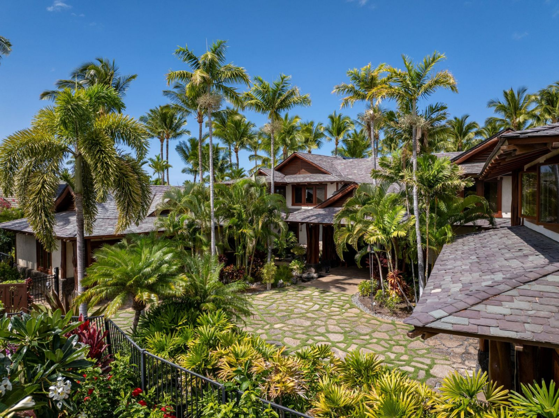 Stone pathways wind through plants and lead toward the covered entry, where the architecture blends natural materials with traditional island design.