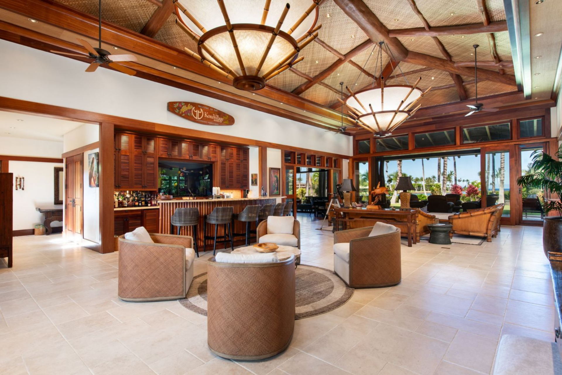 Stepping inside, the home opens into a large great room where structural timbers rise dramatically through a ceiling finished in hand-woven lauhala. 