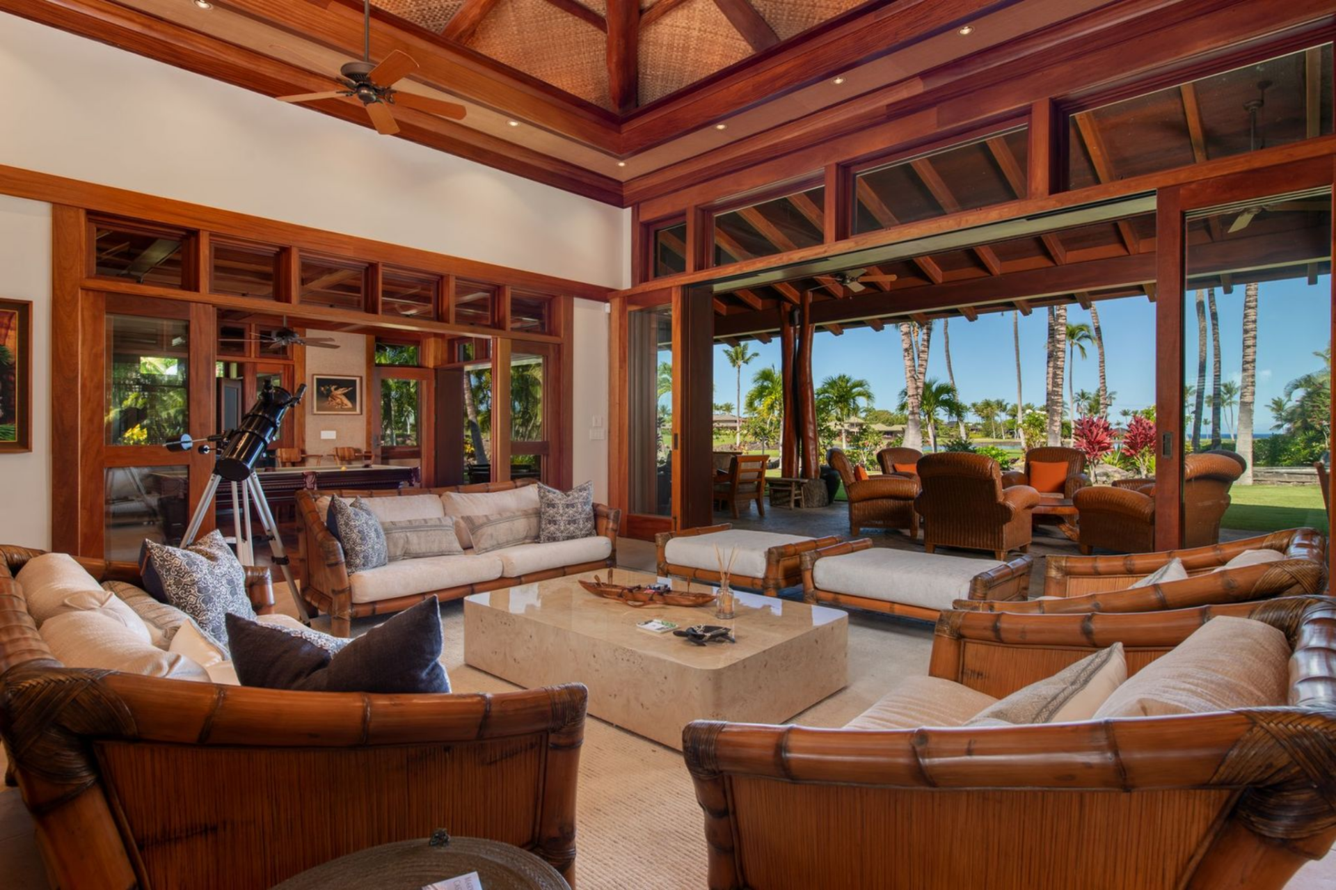 A collection of custom Koa-framed sofas and lounge chairs is arranged around a large stone coffee table, creating a central gathering space that looks out toward the outdoors.