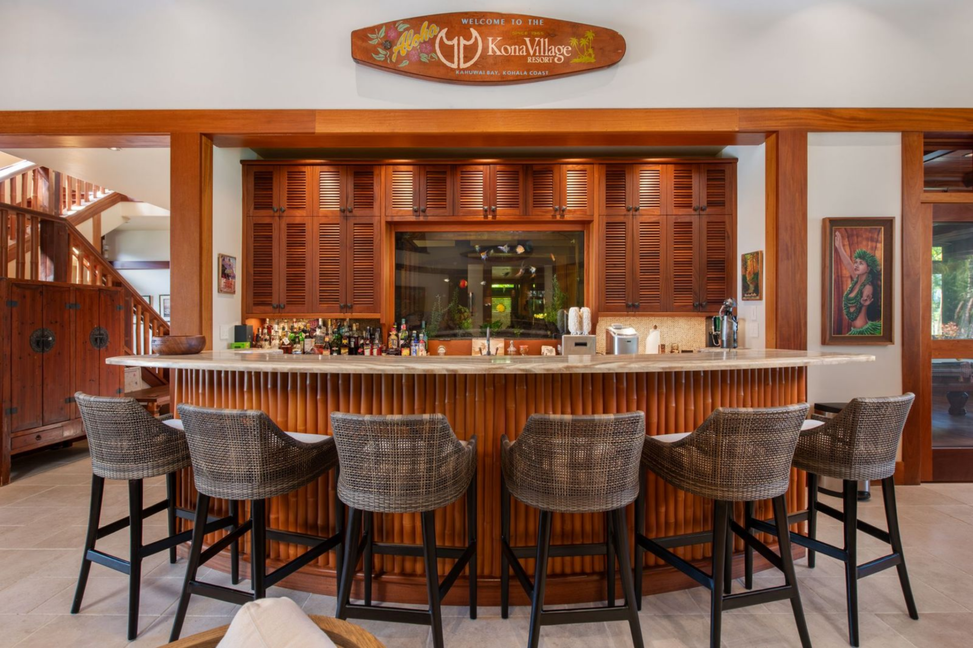 Just steps away within the same open space is a built-in bar finished with warm wood paneling and a stone countertop that stretches across a row of woven barstools.