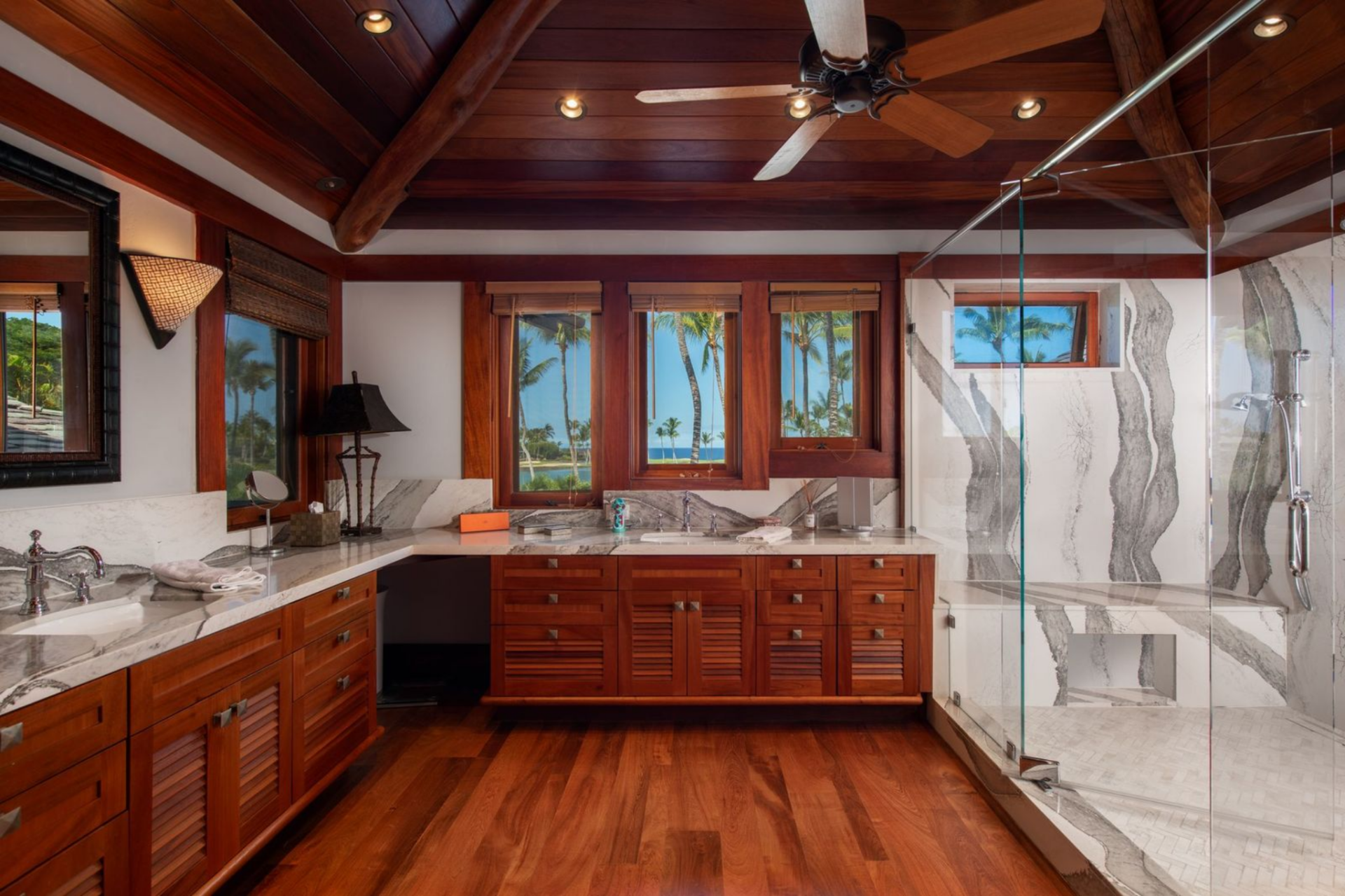 The en-suite bathroom expands the same warm palette with a glass-enclosed shower wrapped in the same dramatic veined stone that lines the countertops of the double vanities.