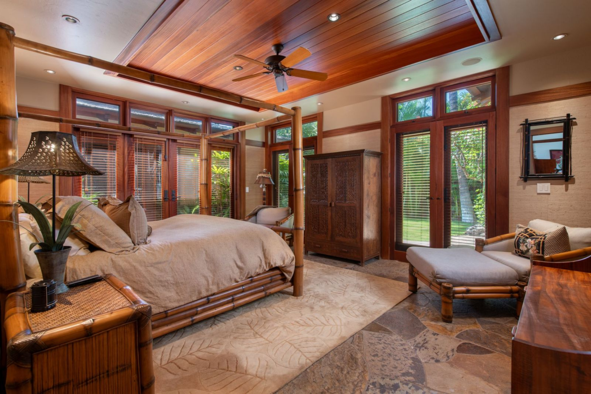 This guest bedroom centers around a bamboo-framed four-poster bed set beneath a warm wood ceiling, all opening directly to the outdoors.