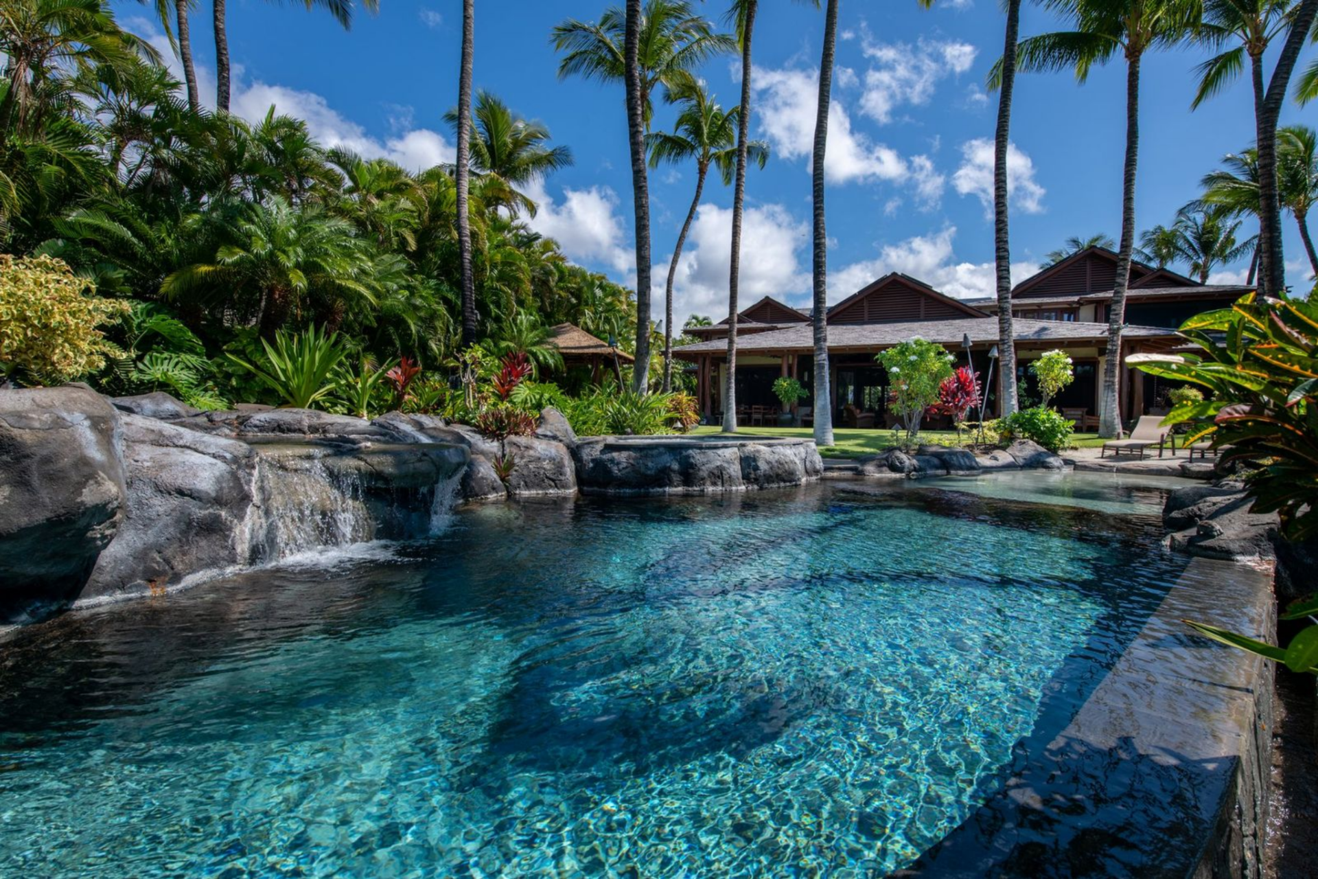 Beyond the covered terraces, the property opens to a resort-style pool and spa surrounded by natural rock features and tropical plants. 