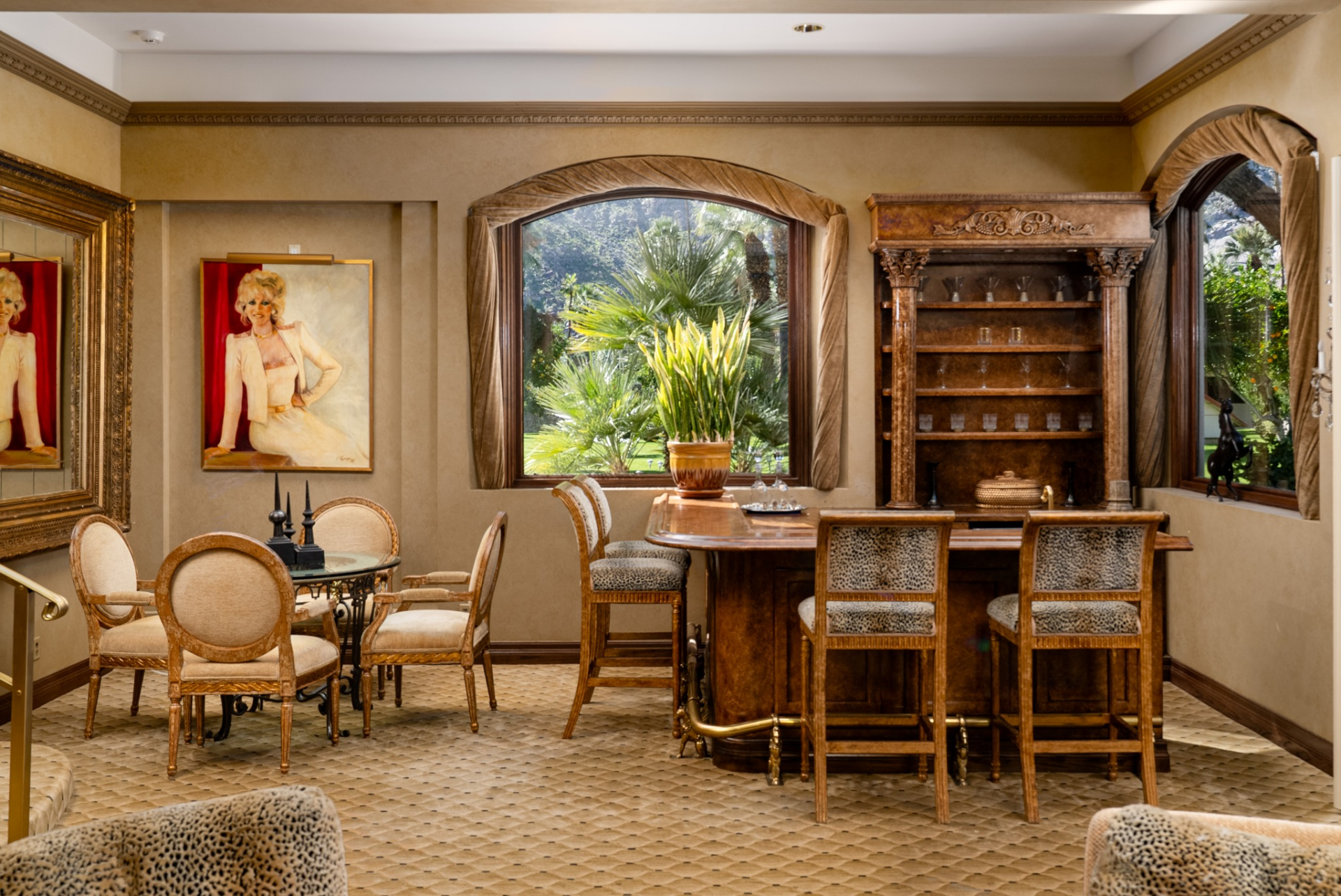 The custom wood bar features a polished countertop with seating for several guests, while a built-in back bar displays glassware and spirits between arched windows that look out to the grounds.