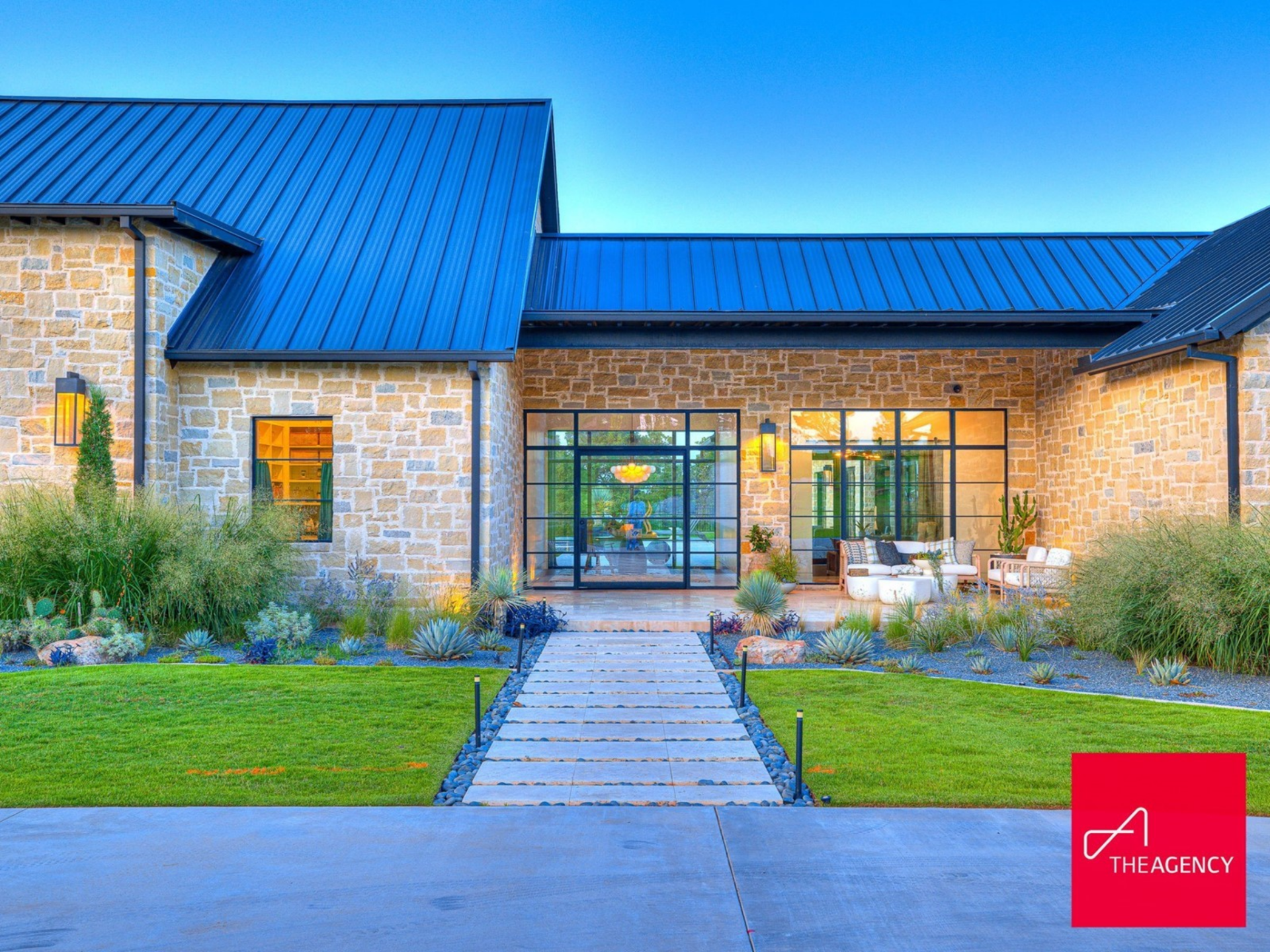 Walking closer, a central walkway of oversized stone pavers leads straight to the glass front doors, framed by native grasses, sculpted shrubs, and low-maintenance plants.