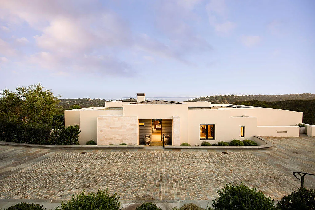 The entrance to the main house is understated, marked by a recessed doorway framed with pale stone and two large planters. 