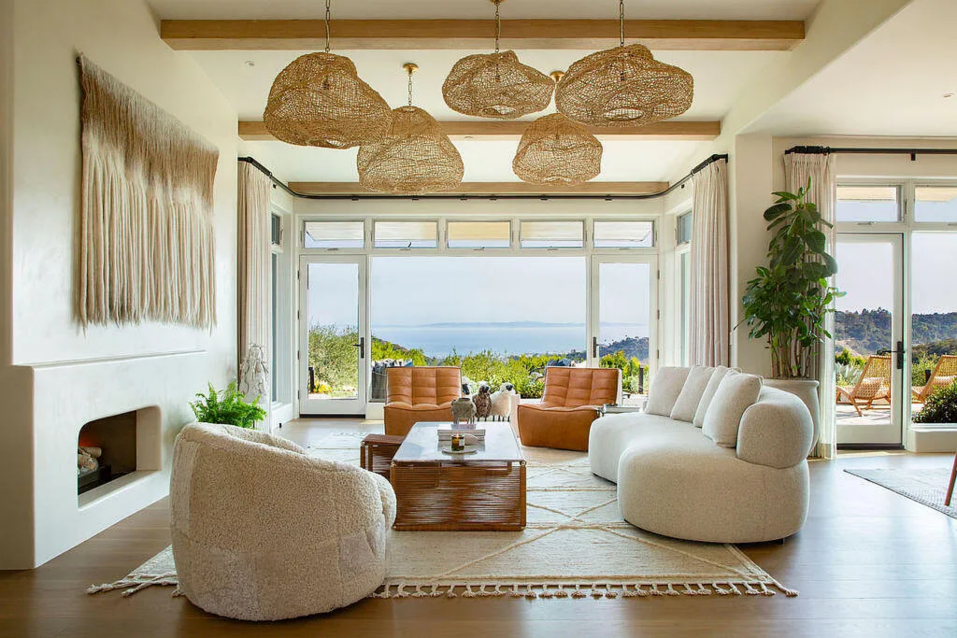 A curved sofa and rounded lounge chairs gather around a low wood coffee table atop a textured area rug, while exposed wood ceiling beams add warmth above.