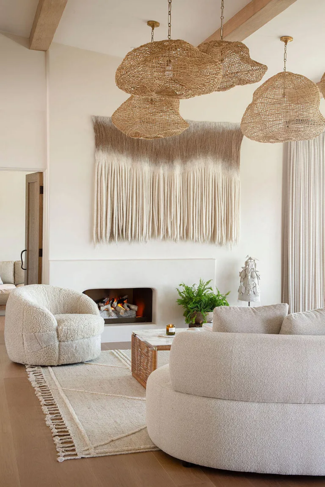 Along one wall, a minimalist fireplace sits beneath a large woven textile installation, and a cluster of sculptural woven pendant lights hangs overhead.