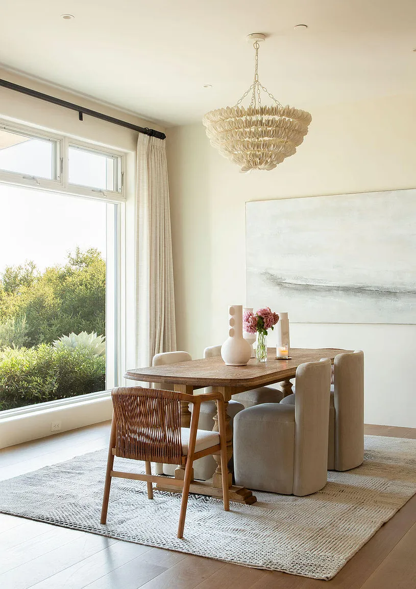 On the opposite side of the living room, the dining area continues the home’s open layout with a rectangular wood dining table surrounded by a mix of upholstered chairs and woven wood seating.