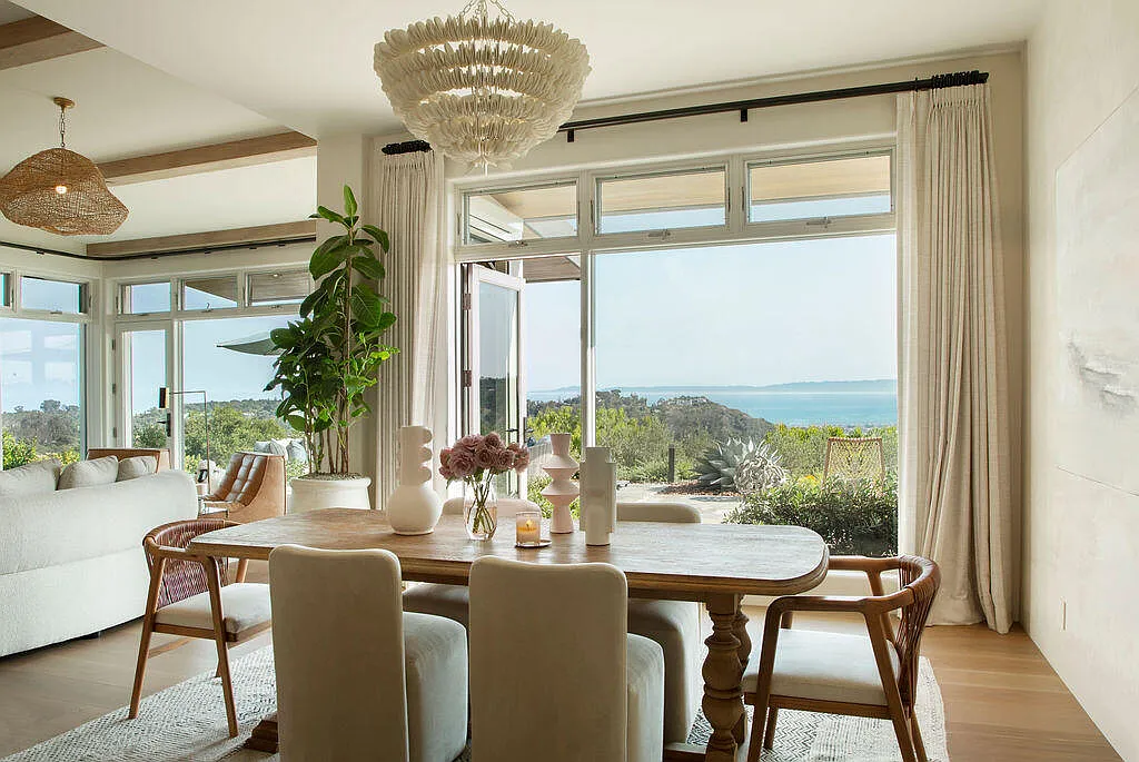 Above the table, a sculptural chandelier made of layered shell-like elements hangs as the focal point, while neutral walls and soft drapery maintain the home's calm, coastal aesthetic.