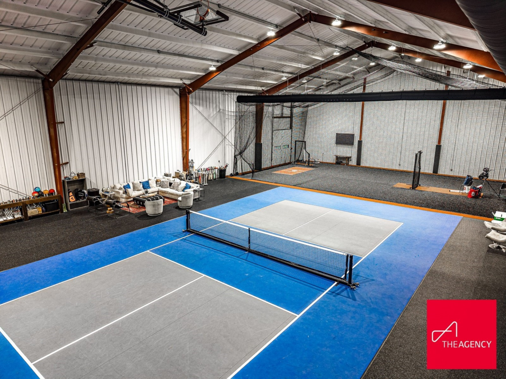 Housed inside a soaring metal-structured building, the full pickleball court features bright blue and gray surfacing with lounge spaces around the perimeter.