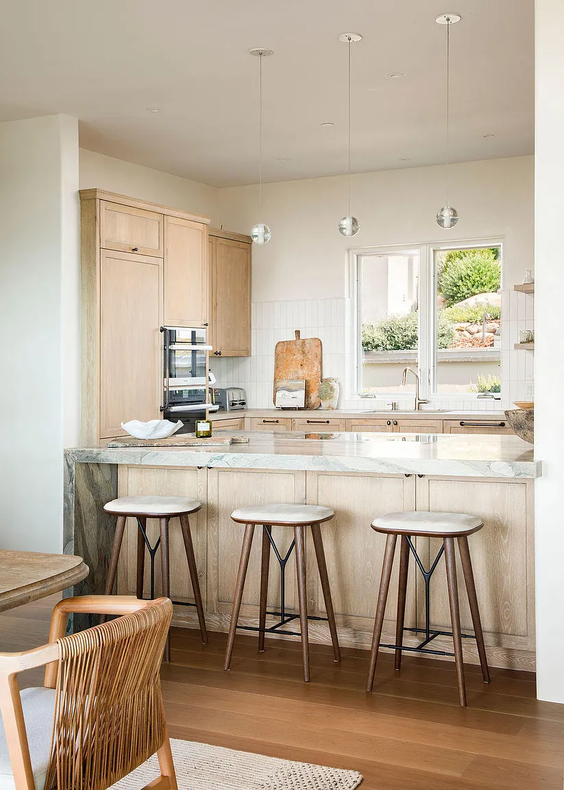 A large central island with a thick stone countertop anchors the space, with seating along one side for casual meals or conversation while cooking.