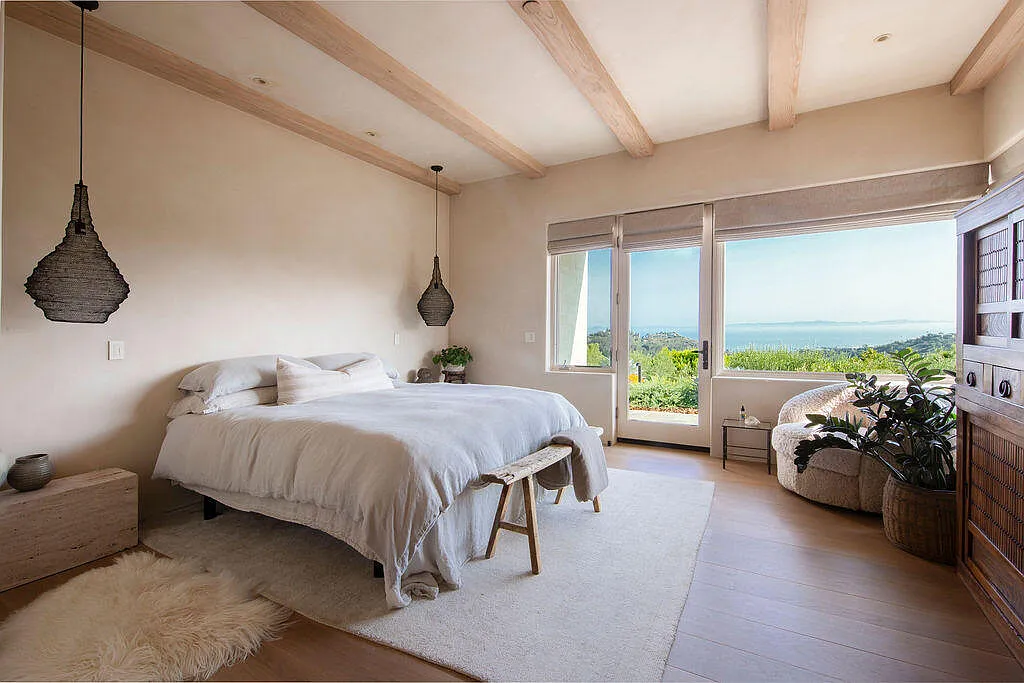 Neutral tones, soft textures, and woven lighting fixtures reinforce the relaxed atmosphere, while a sitting area near the windows provides a quiet spot to take in the scenery.
