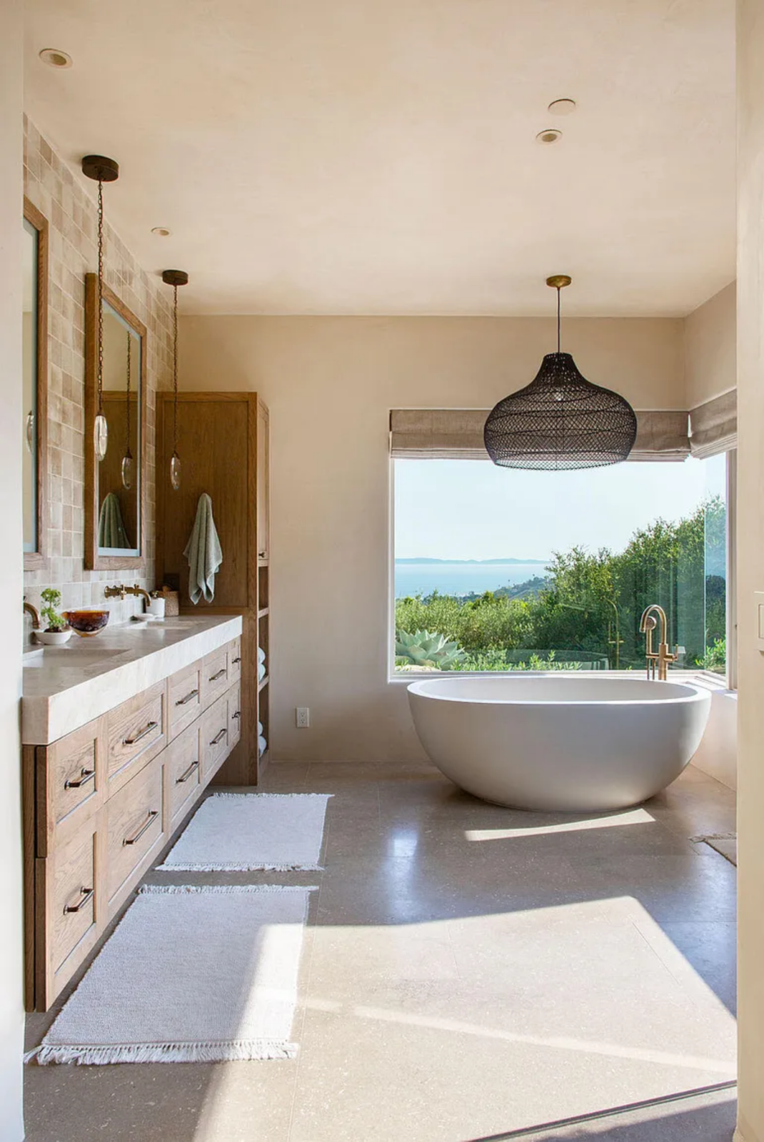 In a corner of the room, a freestanding soaking tub is positioned directly in front of a large picture window, allowing the ocean view to remain the focal point even within the bath.