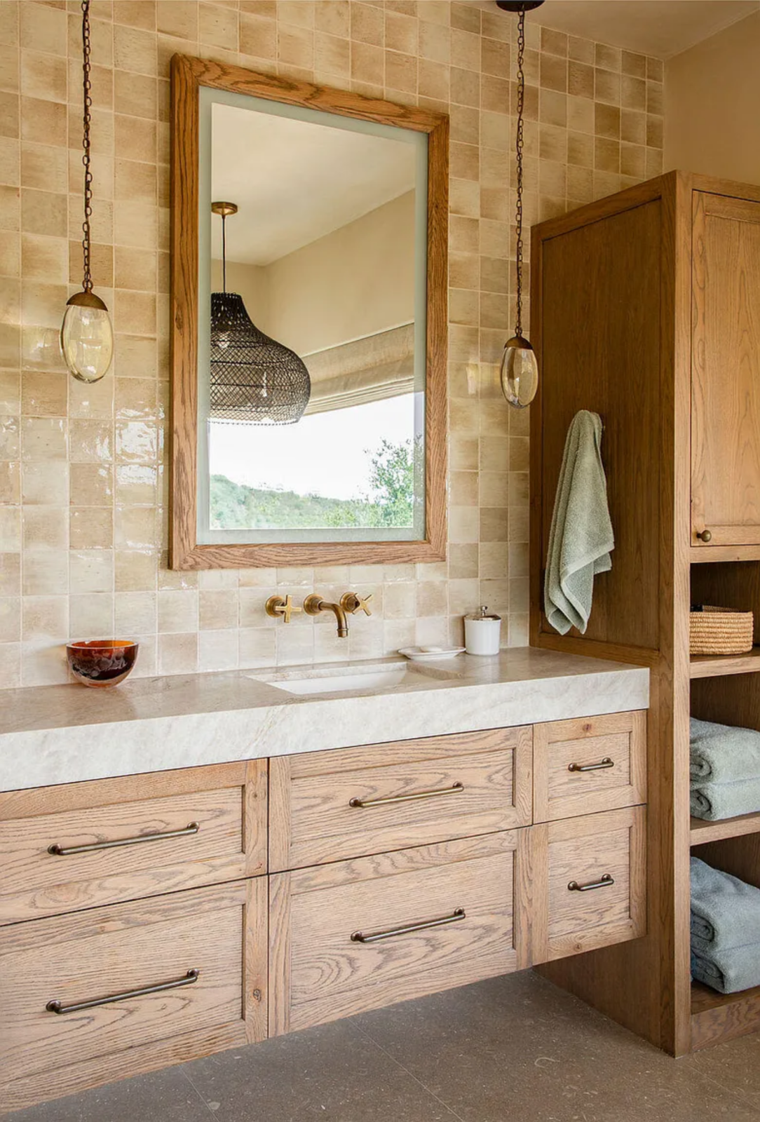 One side of the room features a long double vanity with wood cabinetry and stone countertops that runs beneath framed mirrors and hanging pendant lights. 