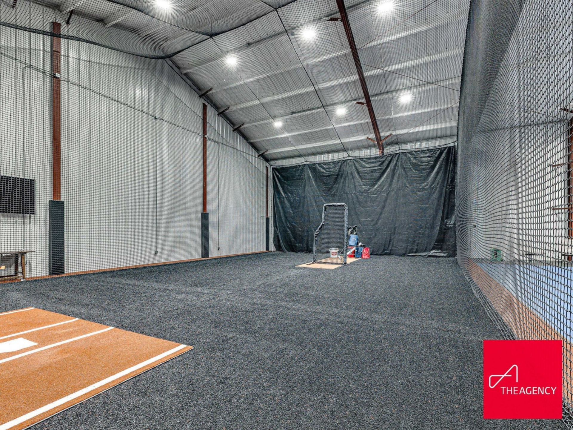 Behind the court, enclosed batting cages stretch the length of the indoor facility, complete with netted walls and pitching areas.