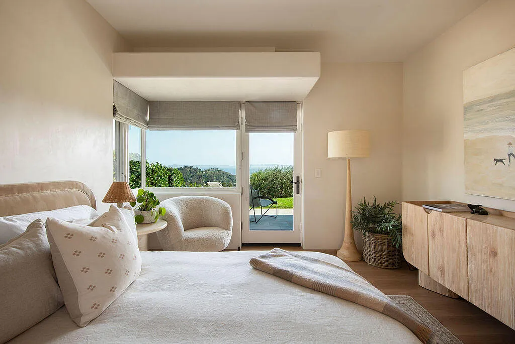 The guest bedroom is set against a large window and glass door, bringing in natural light while opening directly toward the landscape and ocean views.