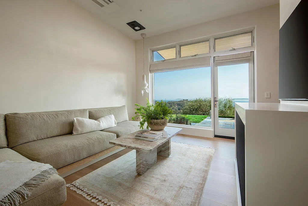 A low-profile sectional sofa is positioned around a stone coffee table and soft area rug, all facing a mounted TV.