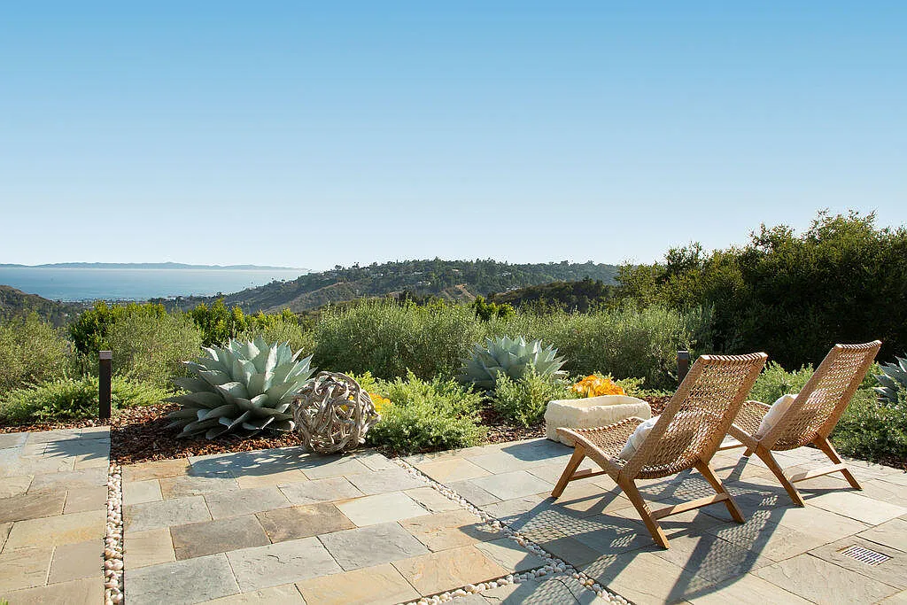 Positioned along the edge of the hillside, the terrace feels closely connected to the terrain, with layered plants of agave, shrubs, and native greenery softening the transition between the architecture and the natural hillside below.