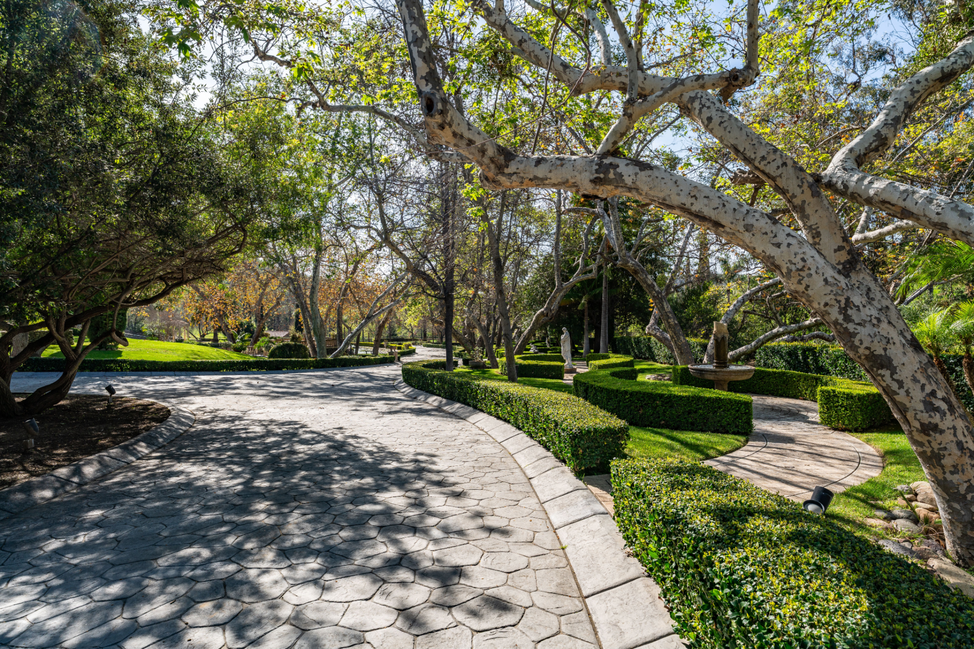 Along the way, sculpted gardens unfold beside the drive, with manicured hedges, stone fountains, and classic statues placed throughout the grounds, reinforcing the European influence that defines the ranch.