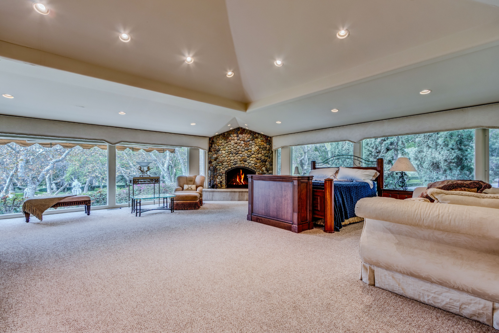 At the center of the space sits a traditional wood bed next to a stone fireplace set into the far wall, creating a natural focal point and adding warmth to the expansive room. 