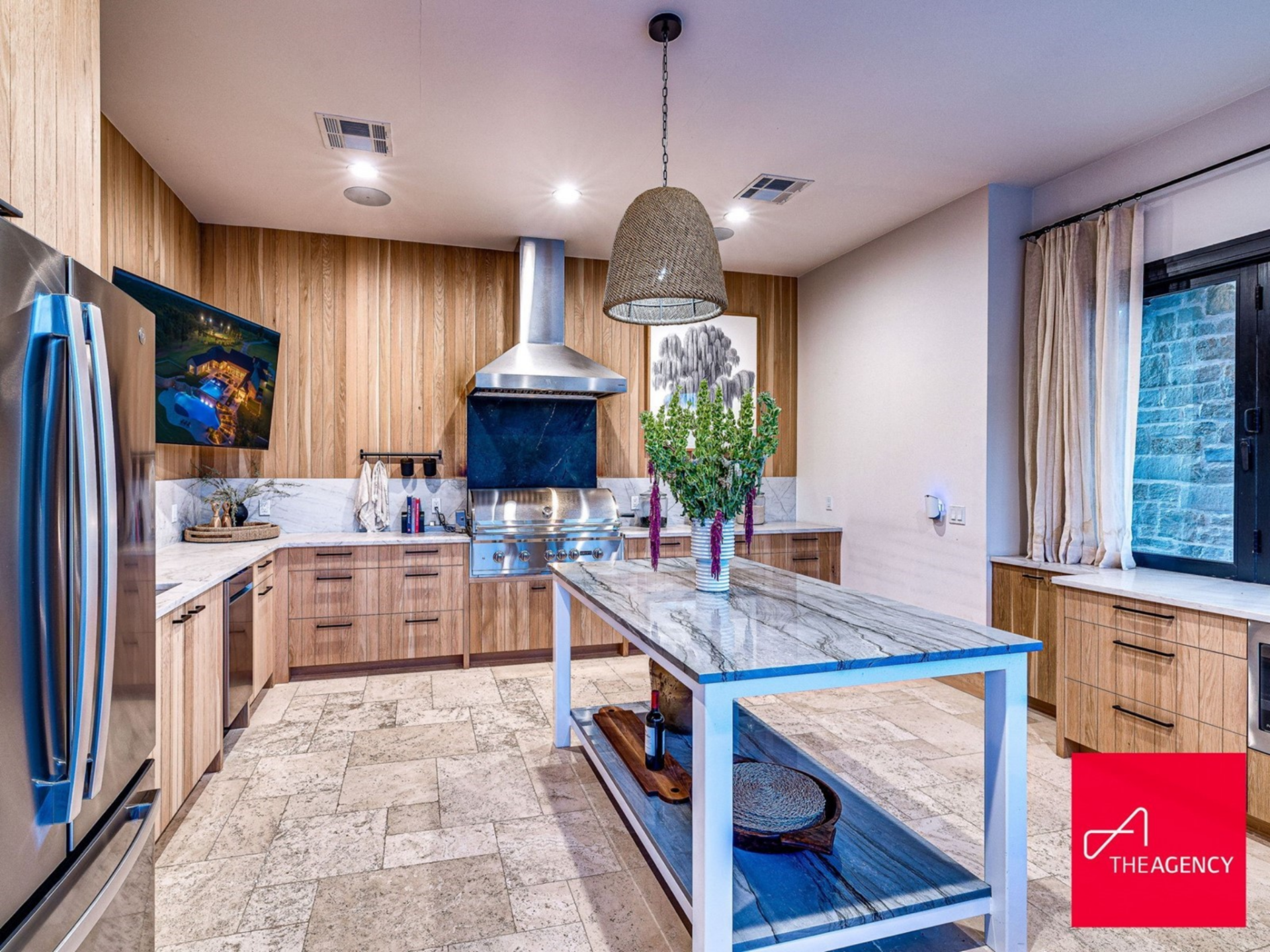 The outdoor kitchen is outfitted with a built-in grill, vent hood, stone countertops, and custom wood cabinetry.